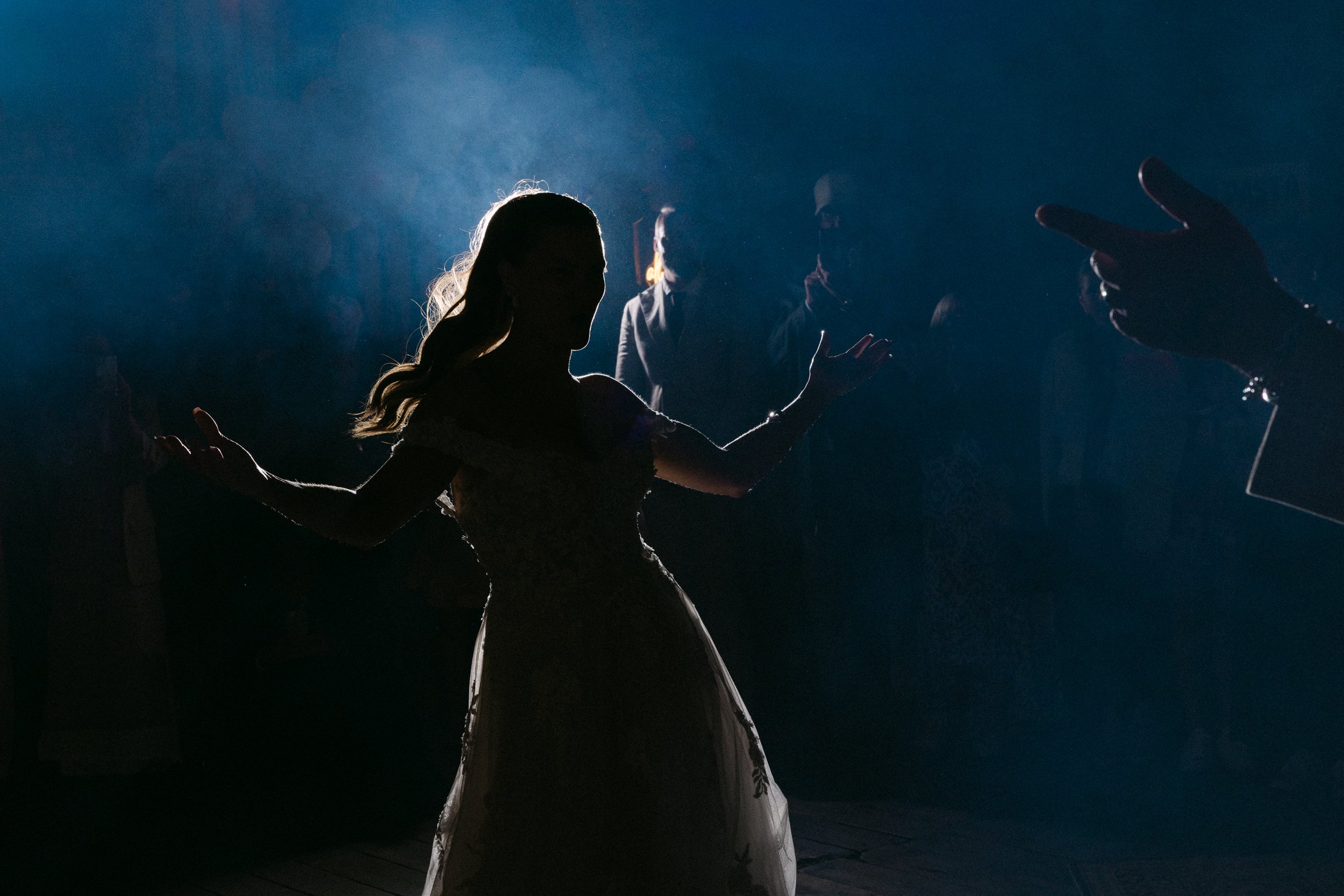 En silhuett av en kvinna som dansar, omgiven av andra personer i bakgrunden, i en mörk miljö med blå ljuskälla.