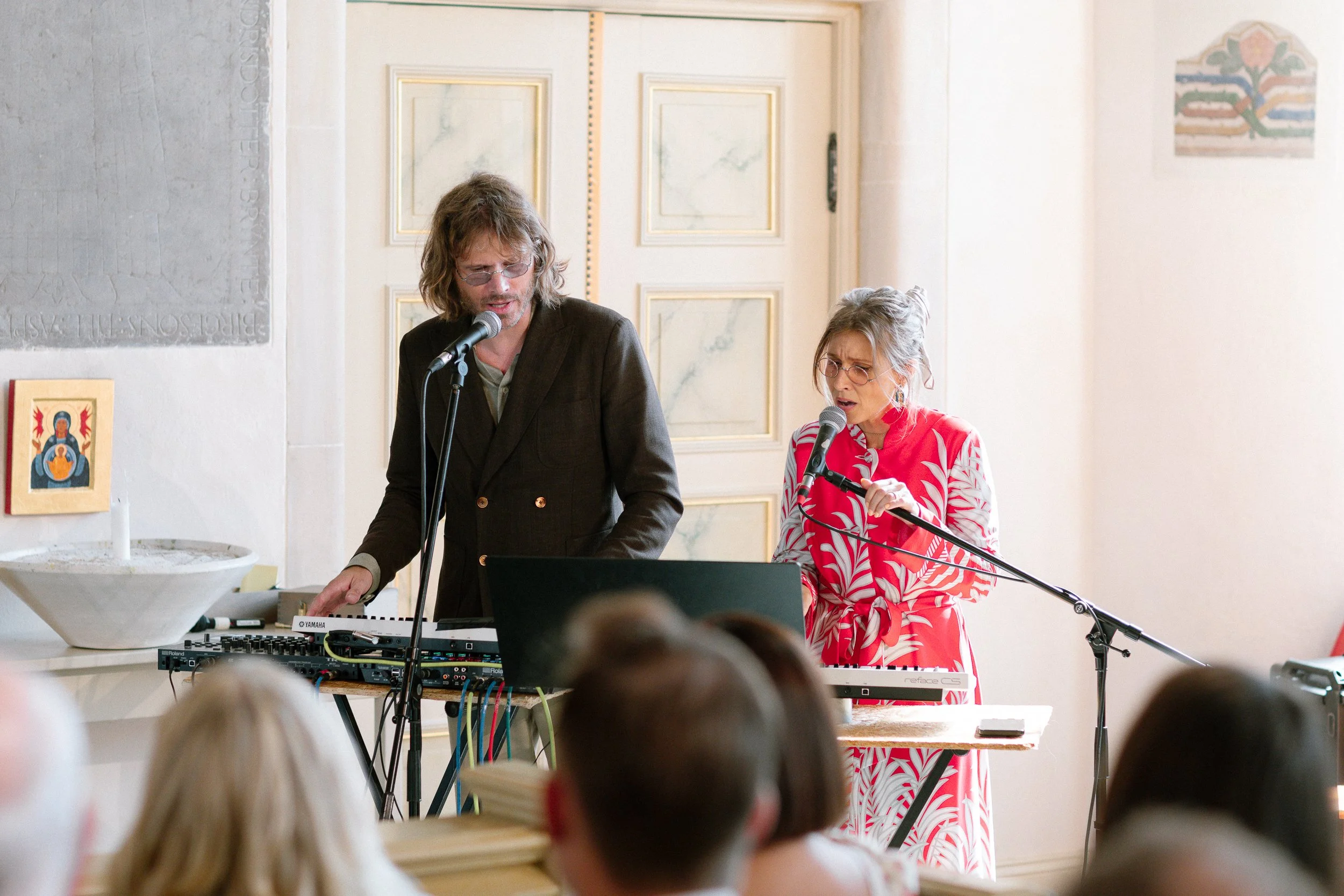 Två personer som framför musik på scenen under ett event, med publik i förgrunden.  Av Sofia Wilhelmina bröllopsfotograf i Stockholm.
