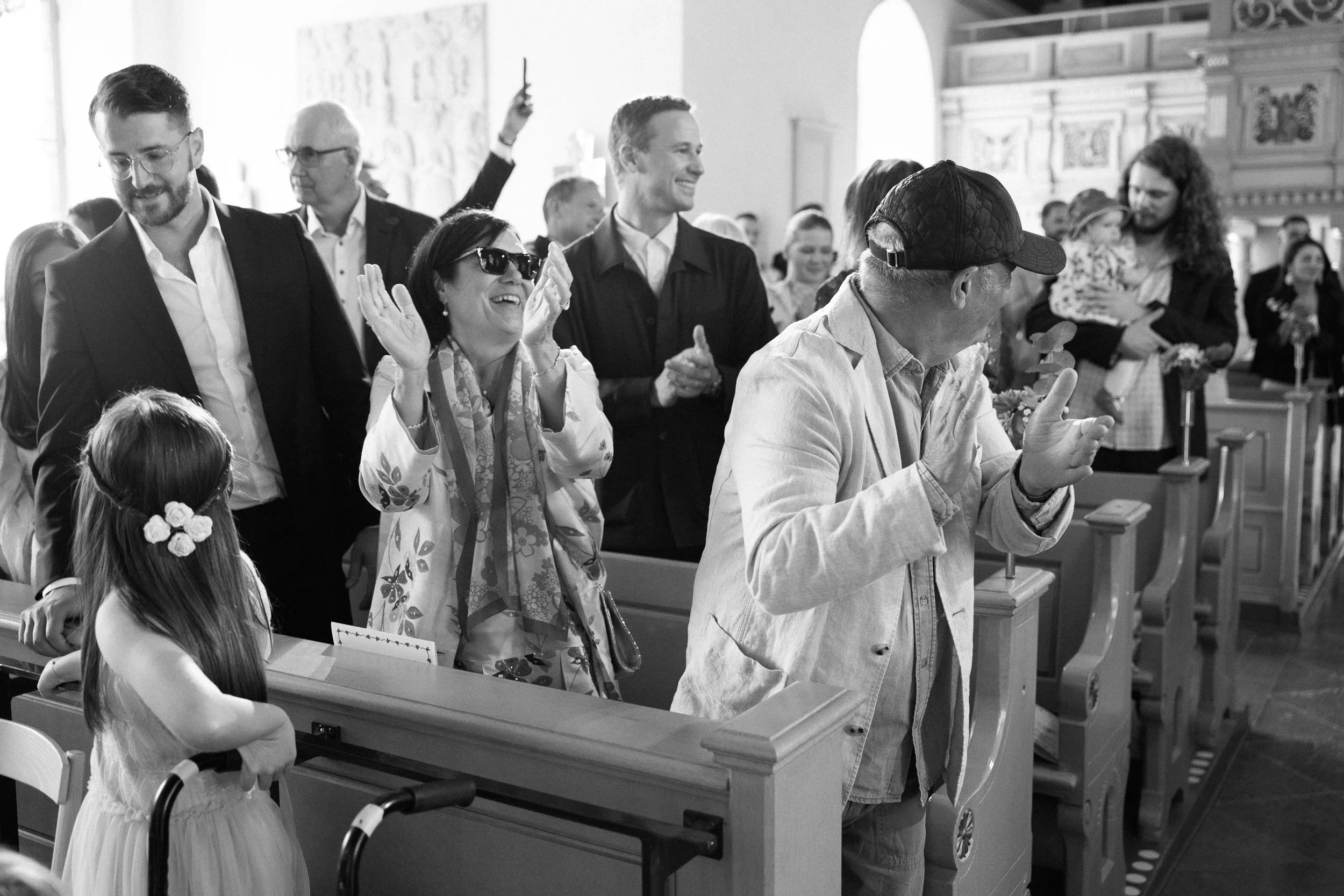 Människor i kyrka som skrattar och applåderar under en ceremoni, svartvit bild.