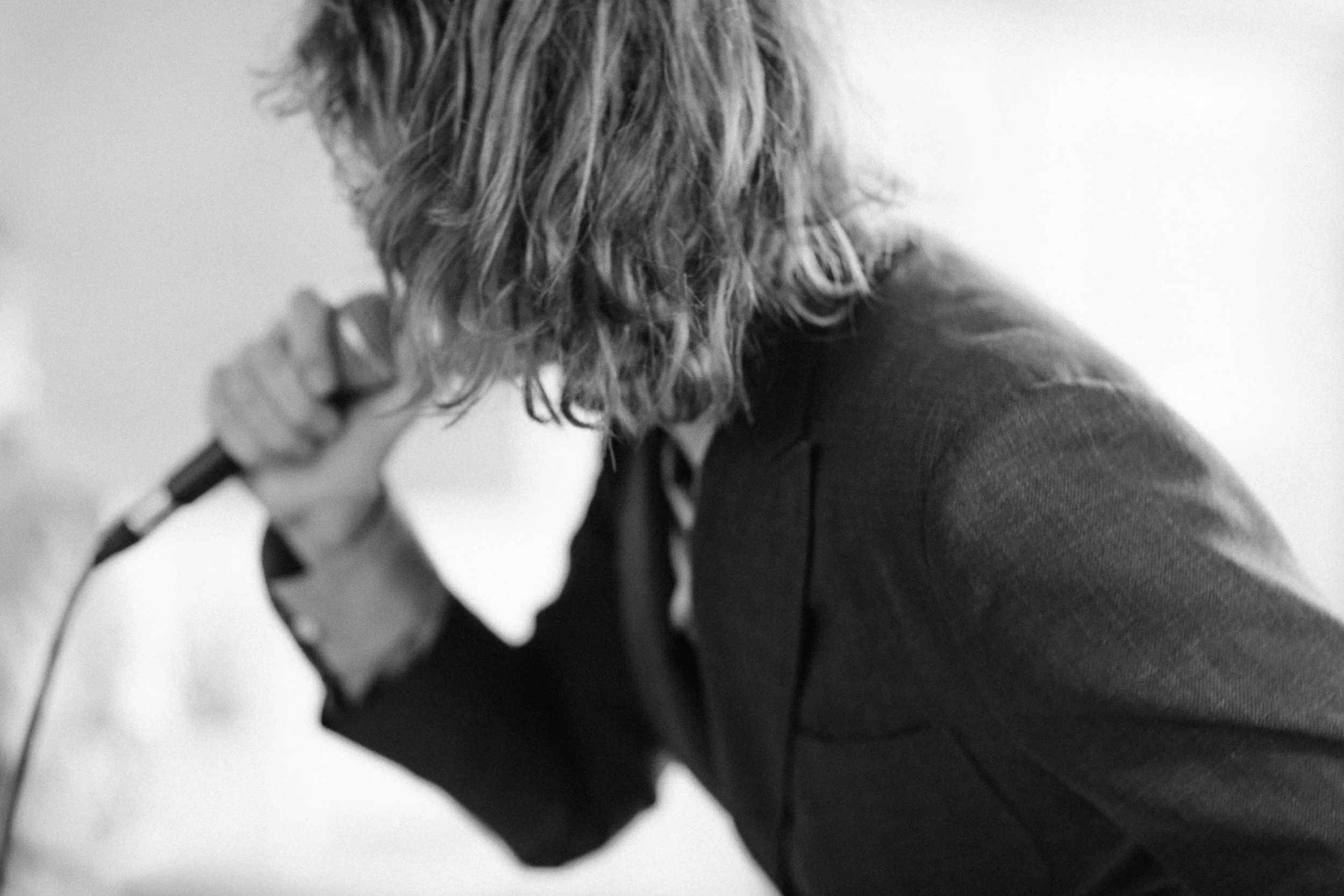 Person med långt, vågigt hår som håller en mikrofon nära munnen. Personen är klädd i en mörk blazer.  Av Sofia Wilhelmina bröllopsfotograf i Stockholm.