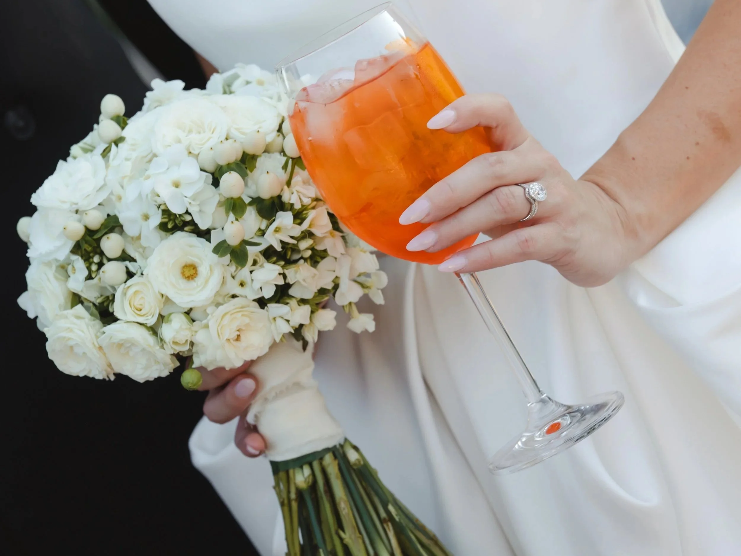 Bride holding a white rounded bouquet and an aperol spritz