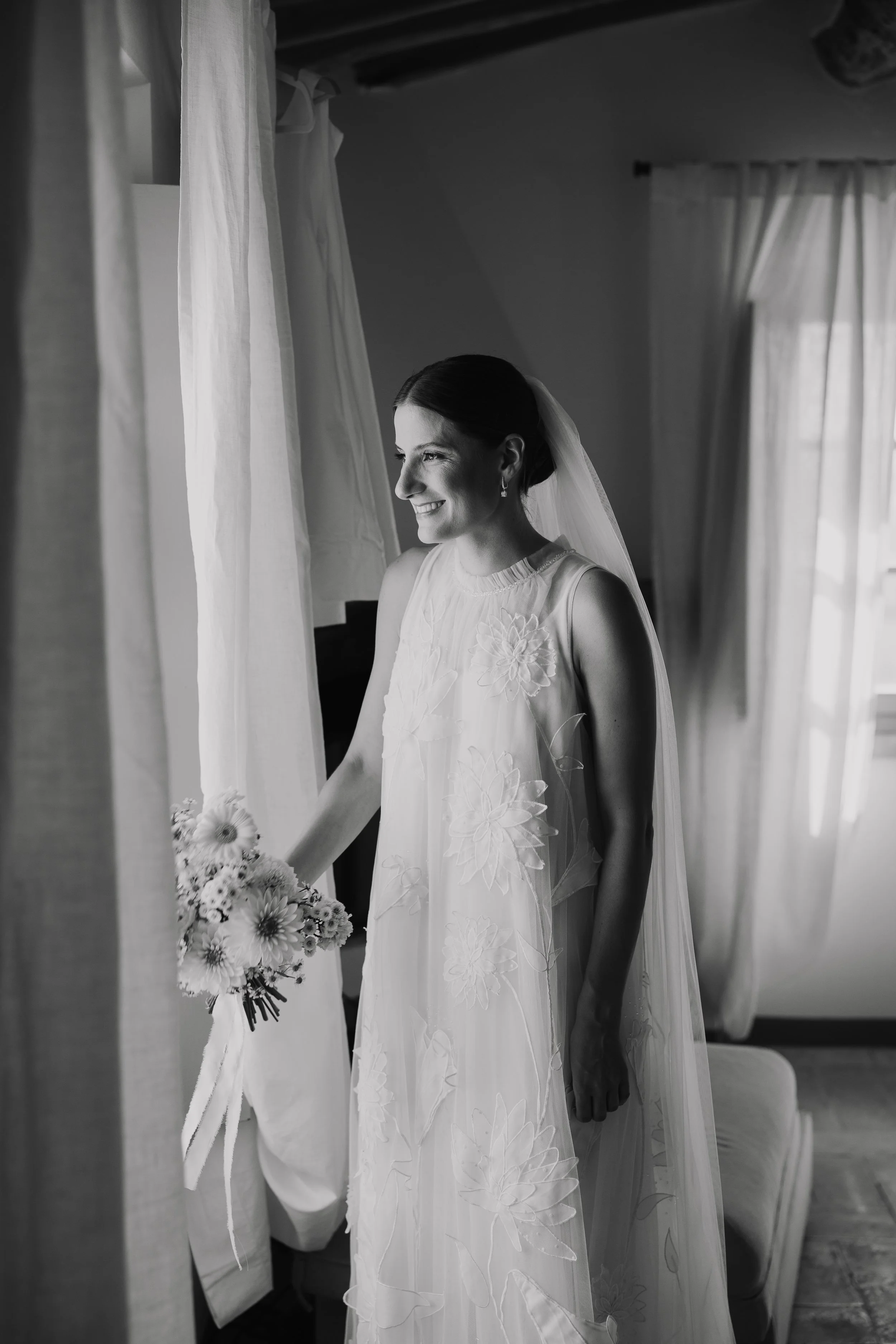bride waiting at the window before the ceremony with bouquet in her hand