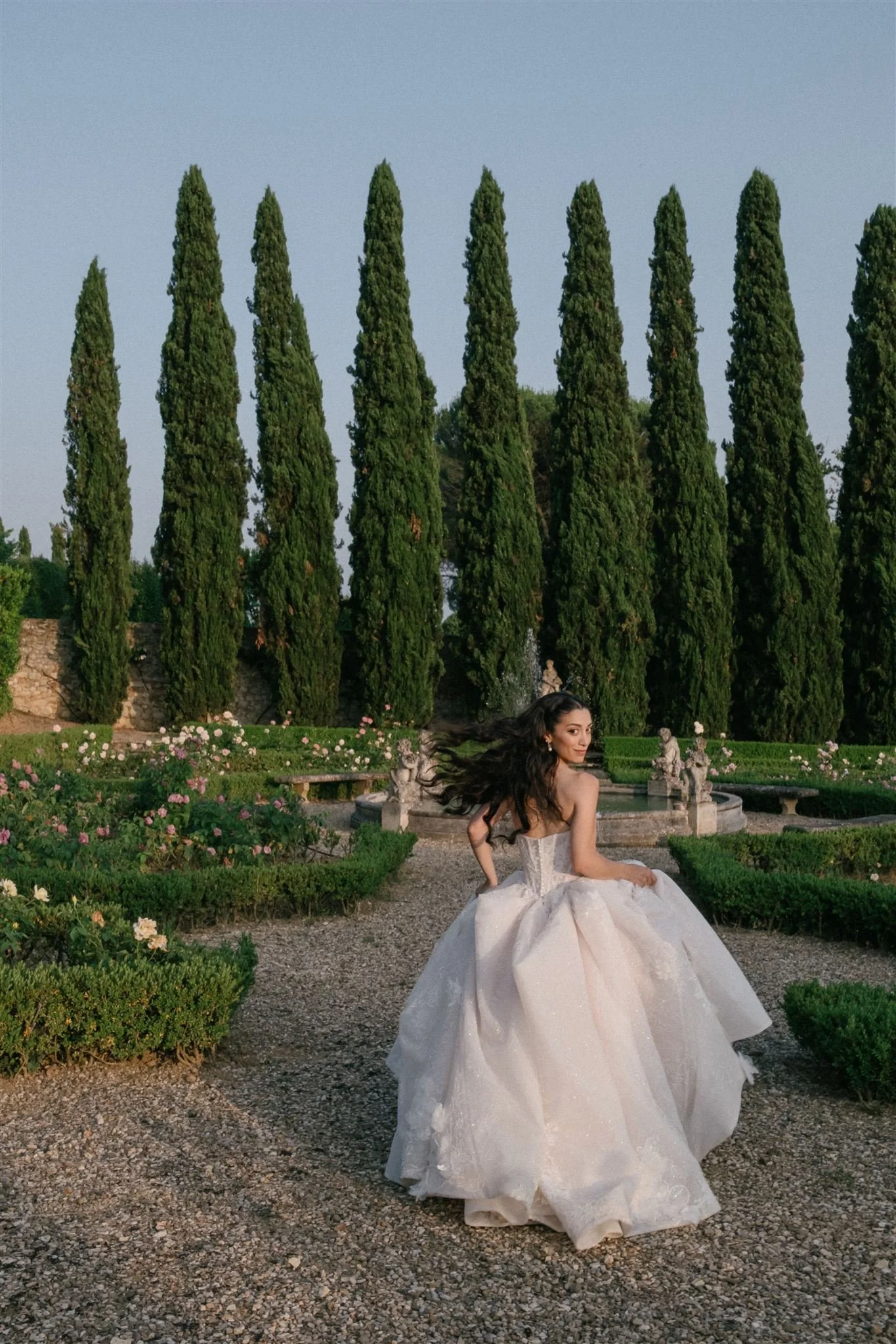 Bride walking through Italian garden with cypress trees