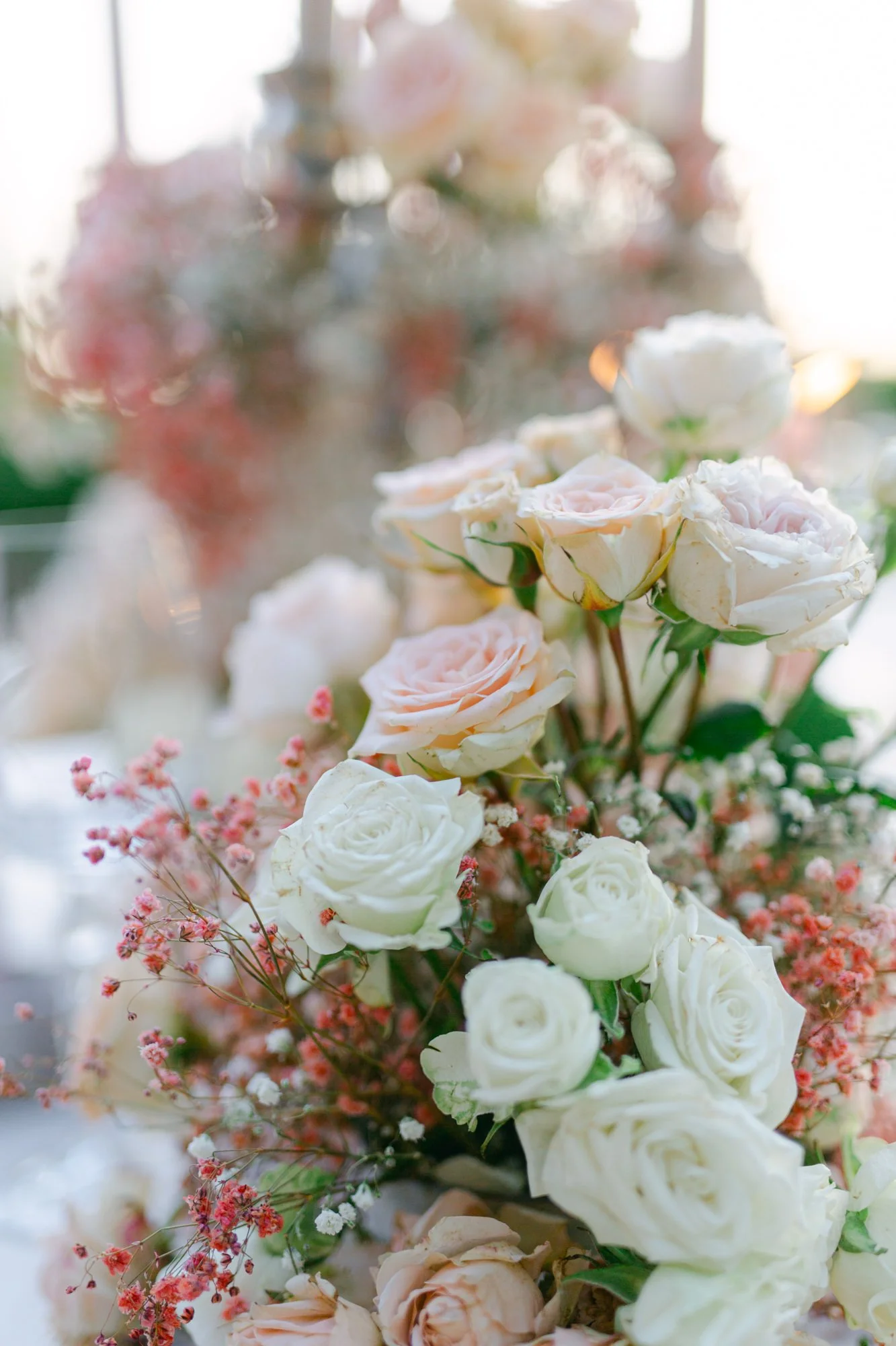 Close-up of a bouquet of pale pink and white roses with small pink and white filler flowers, background blurred with light from a window.