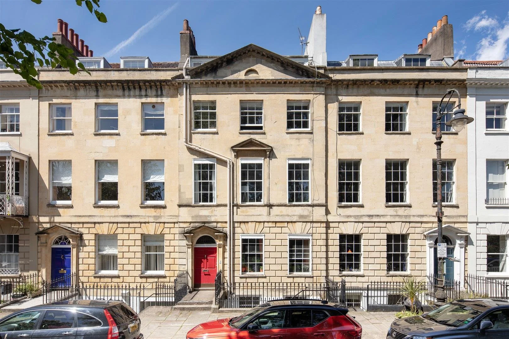 Row of three-story townhouses with colorful doors, parked cars in front, and a clear blue sky above.