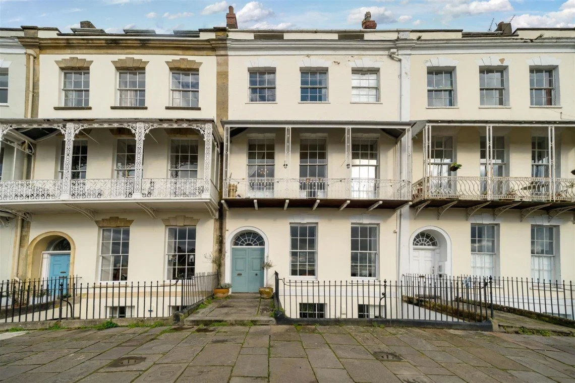 Row of historic townhouses with iron balconies and pastel colored doors in a city neighborhood.