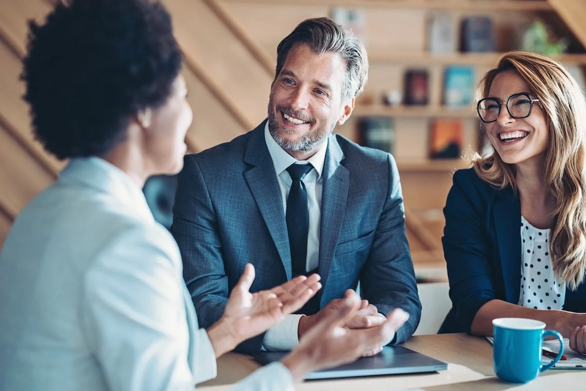 a man and two women in professional attire smile during a business meeting