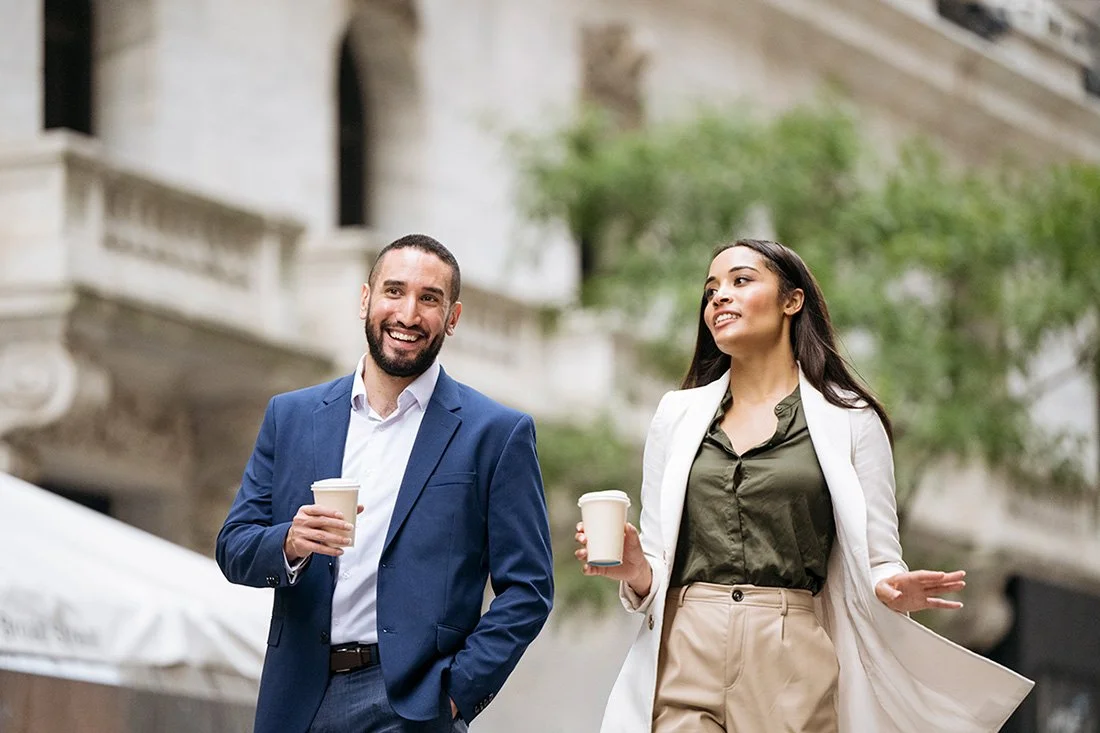 male and female professionals walking on a city sidewalk with coffee in their hands