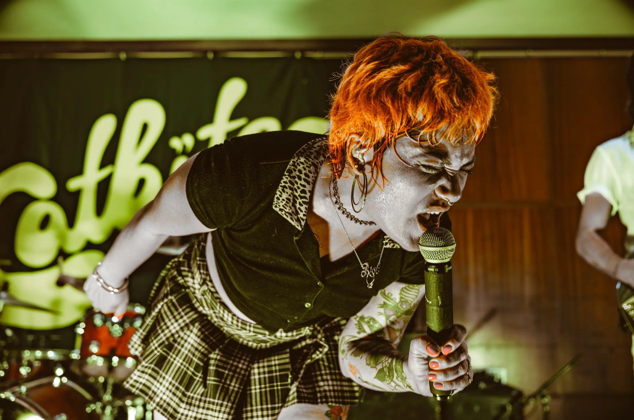A woman singing passionately into a microphone during a live performance, with bright stage lighting and musical instruments in the background.