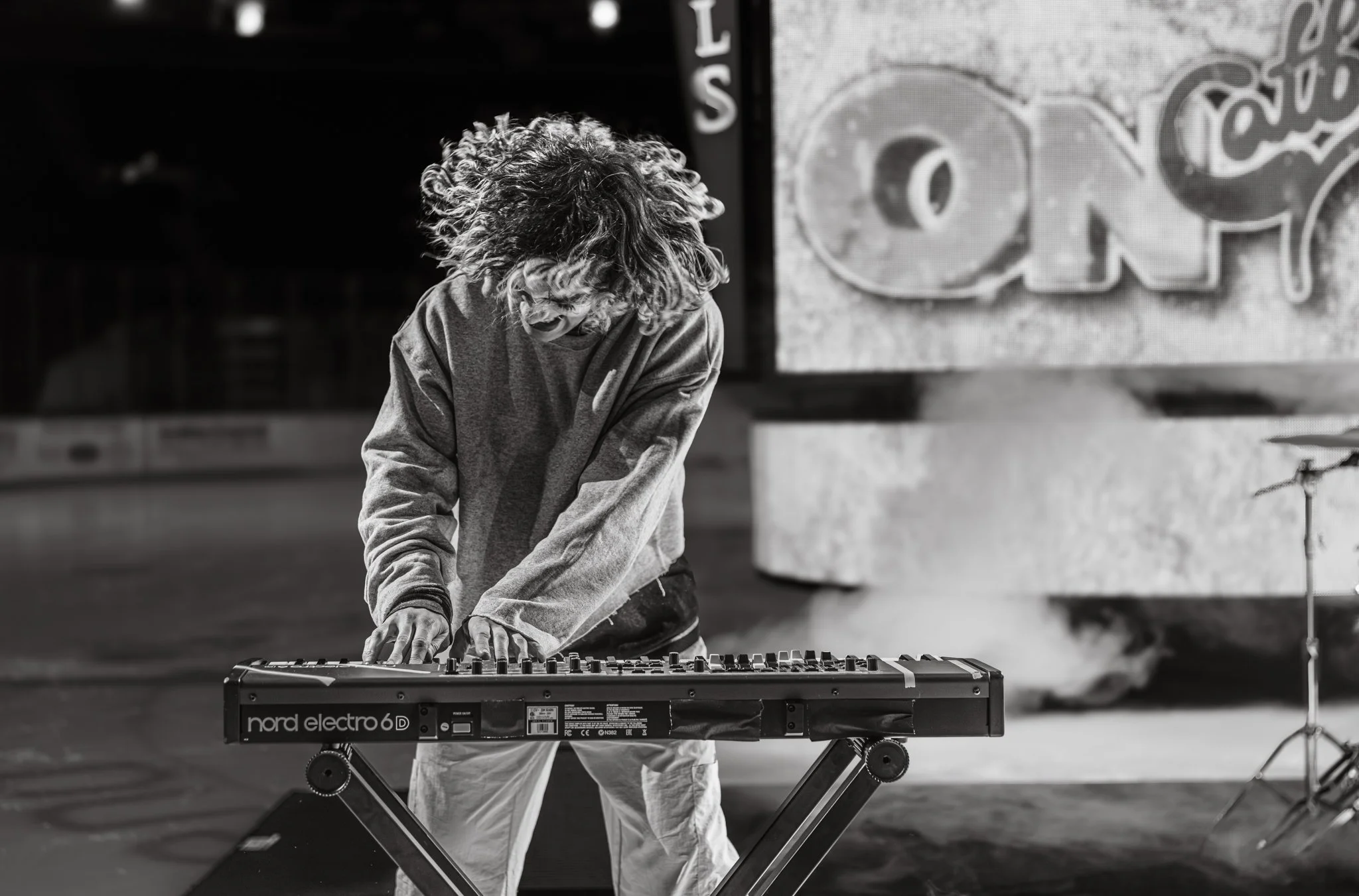 A musician with curly hair playing a Nord Electro 6D keyboard on a stand, performing in a studio or stage setting.