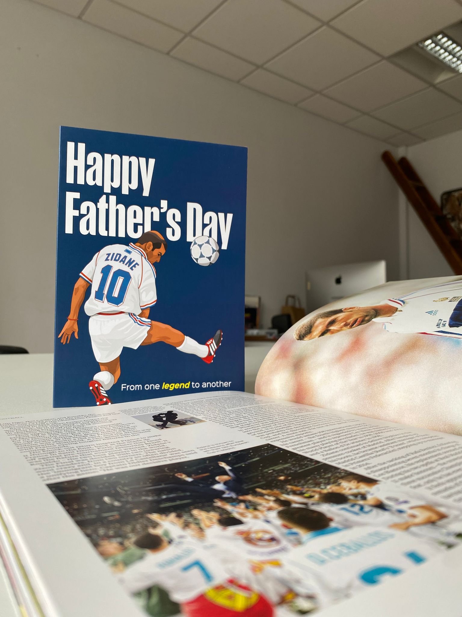 Father's Day greeting card with a soccer player illustration and the message 'Happy Father’s Day' on a table alongside magazine pages and a glossy magazine.