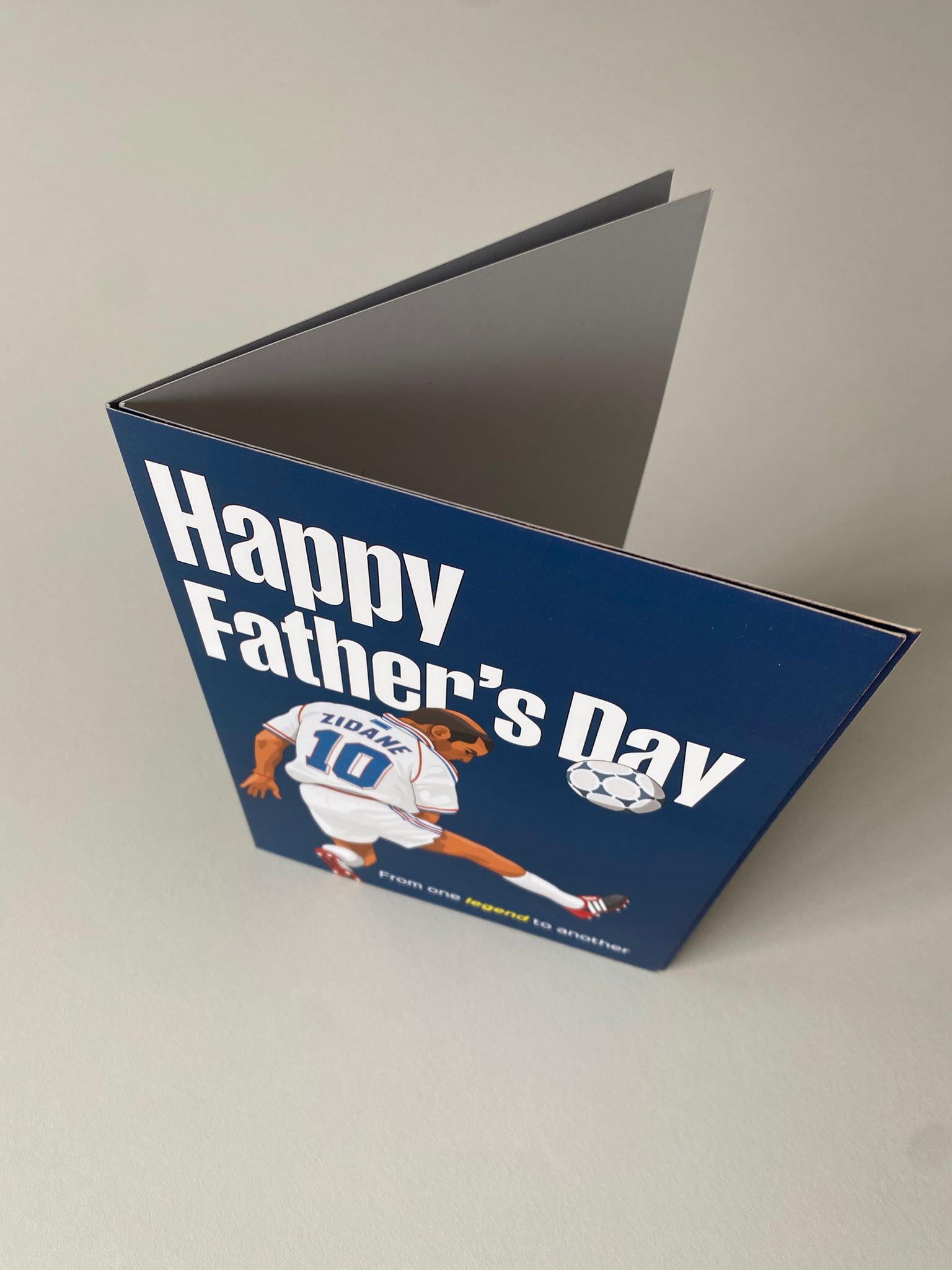 A greeting card with a blue background says "Happy Father's Day" and features a cartoon soccer player in a white uniform with the number 10, kicking a soccer ball.