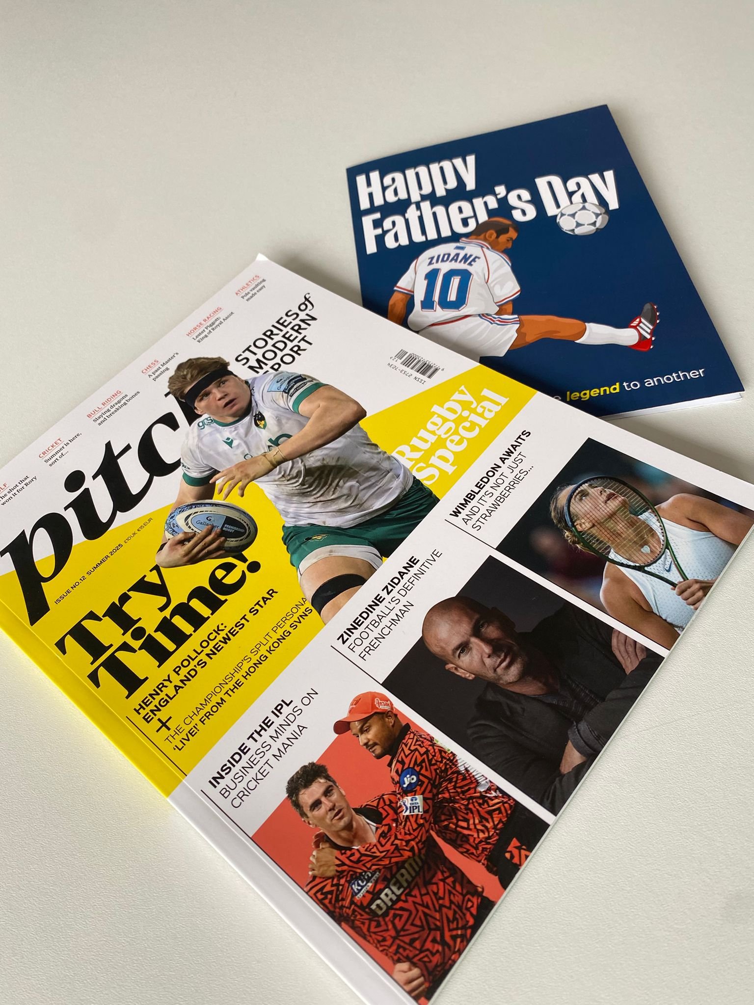 A magazine and a Father's Day card on a white surface. The magazine features a rugby player holding a ball, and the card has a football player in a jersey with “10” on the back and the text "Happy Father’s Day."