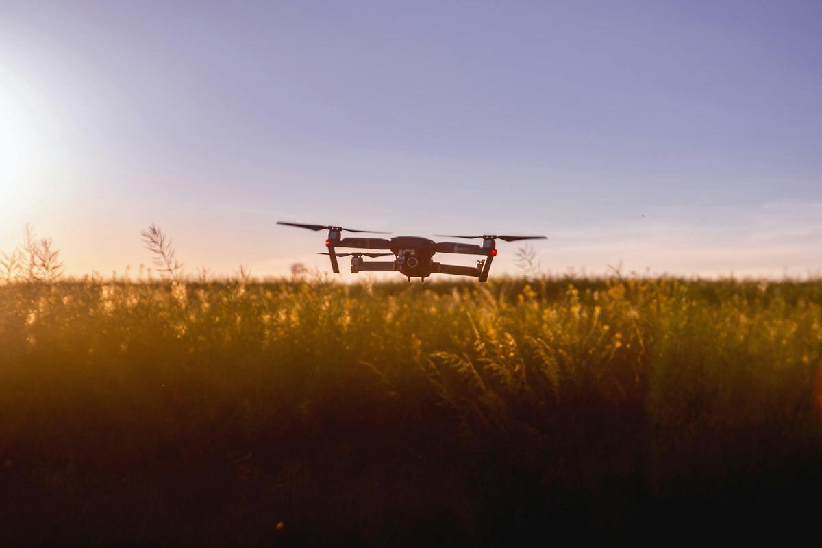 A drone flying over a field during sunset or sunrise.