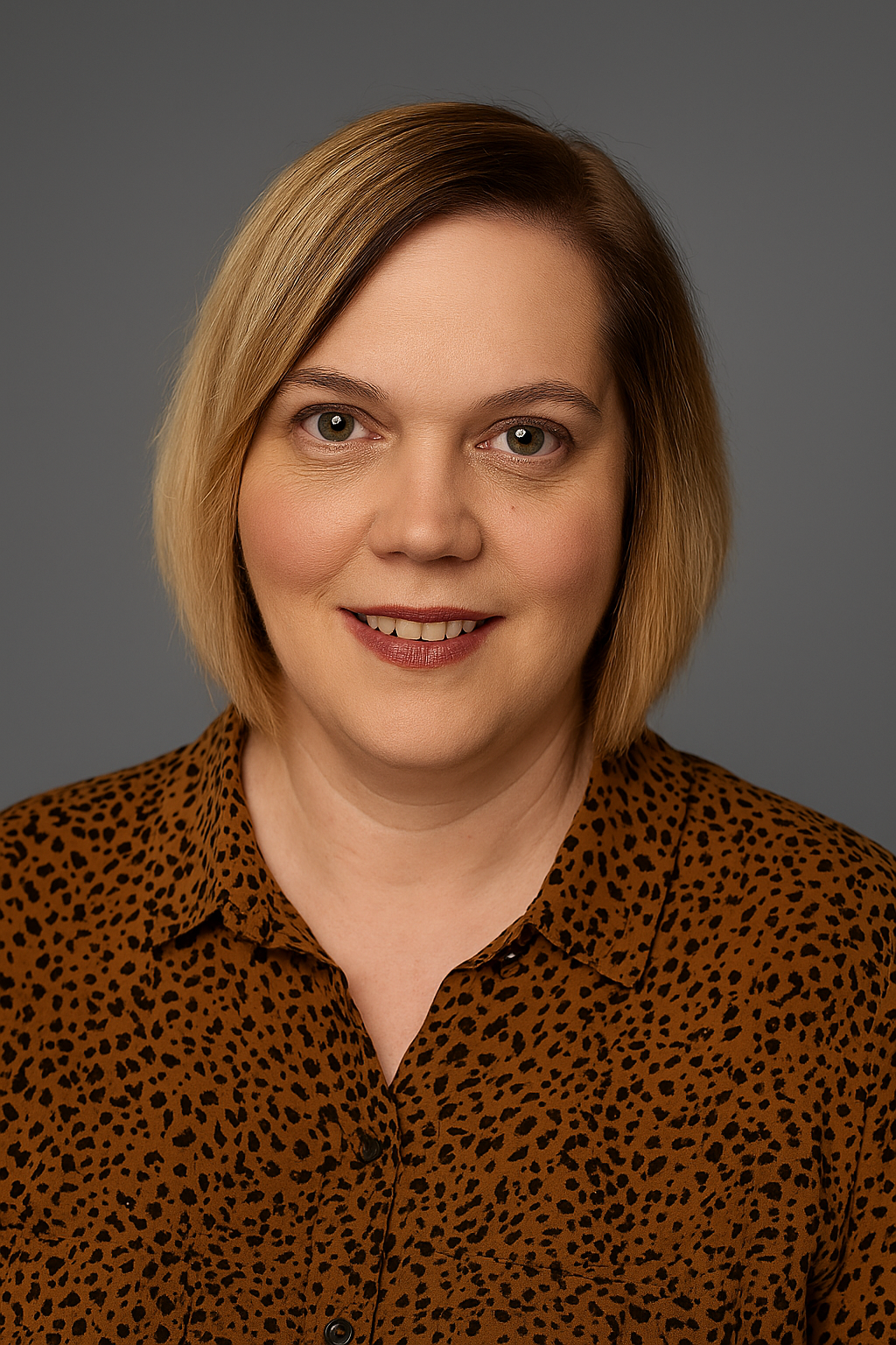 A woman with shoulder-length blonde hair, light-colored eyes, wearing a brown leopard print blouse, smiling against a gray background.