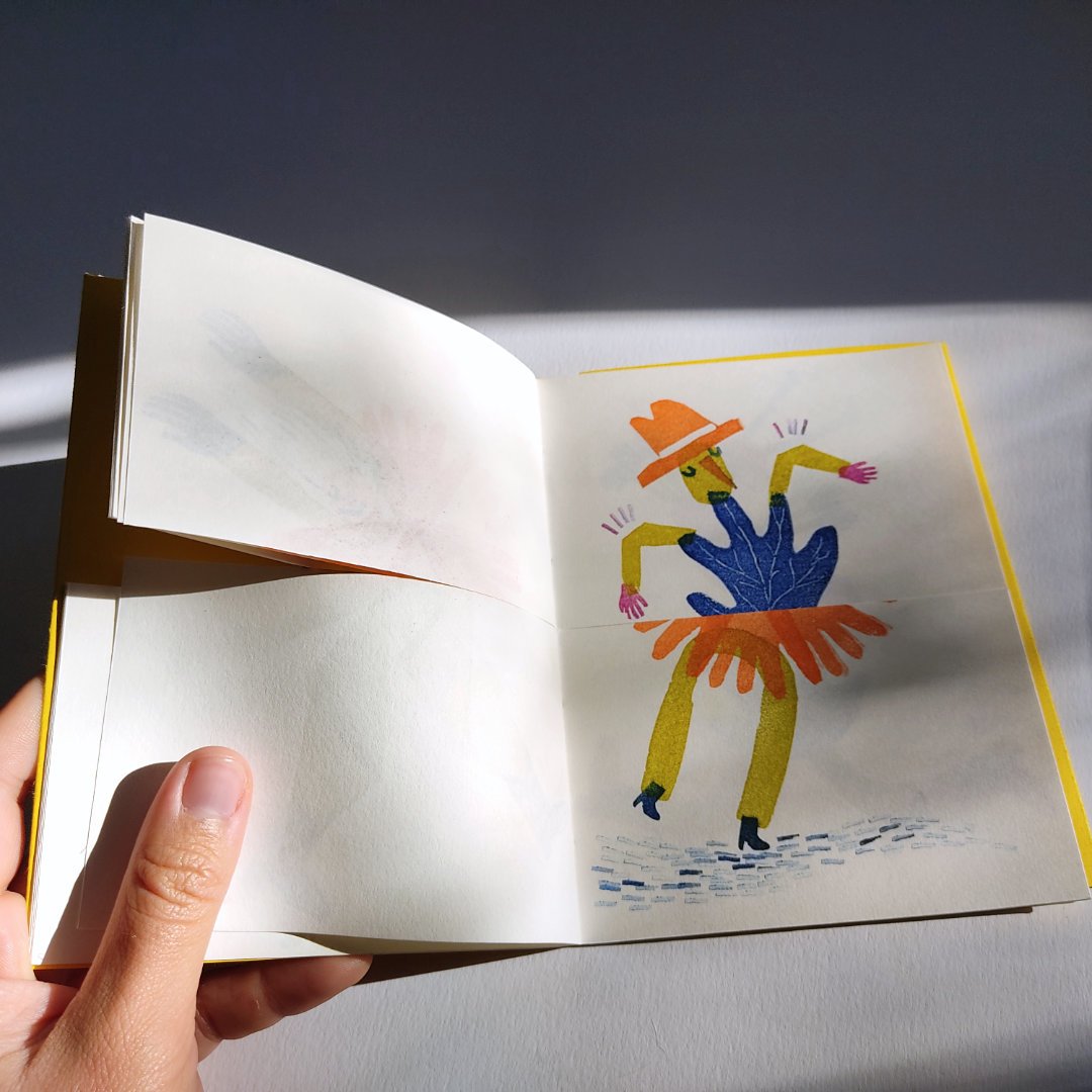 Livret ouvert avec illustration artistique colorée d'une figure humanoïde portant un chapeau et une jupe, tenant les bras écartés.