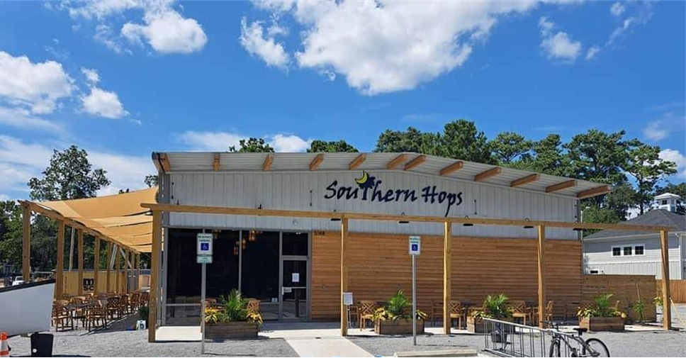 Exterior of Southern Hops restaurant in Murrells Inlet SC with wooden facade, outdoor seating, and a shaded patio area, under a blue sky with a few clouds near Myrtle Beach, SC