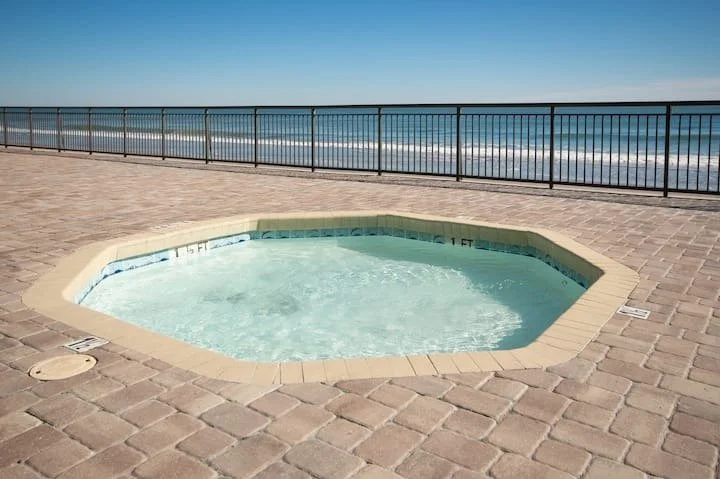 Small hot tub on a beachside promenade with ocean and clear sky in the background.