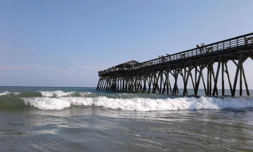 Photo of Garden City Pier extending over the ocean with waves and a clear sky in Garden City, SC near Myrtle Beach, SC