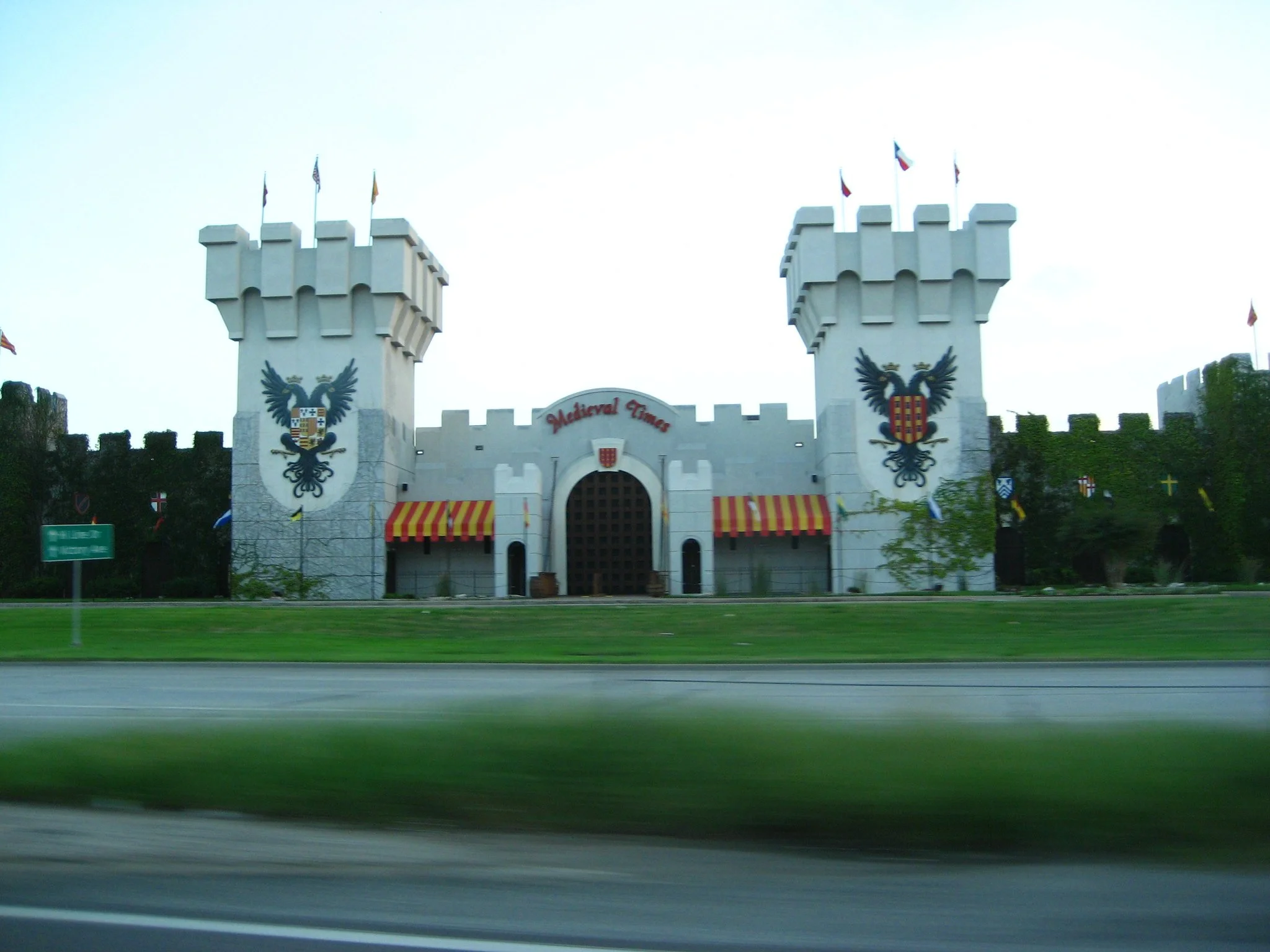 A castle-themed structure with two towers, each adorned with heraldic eagle shields, and a central entrance with striped awnings, labeled 'Medieval Times' near Myrtle Beach, SC