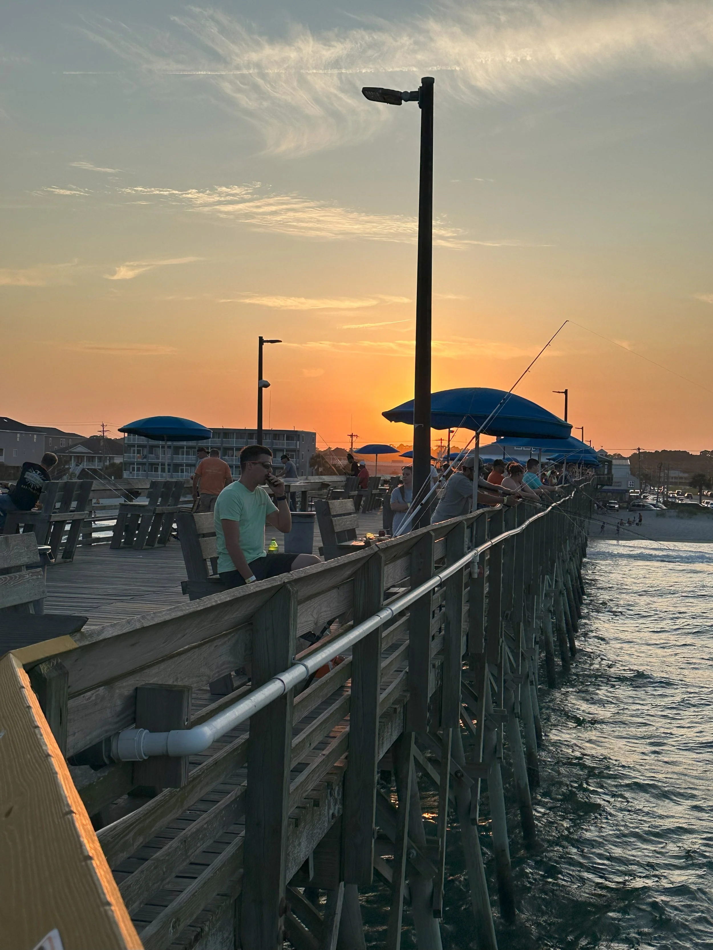 People fishing off The Pier at Garden City during sunset with some benches and umbrellas along the pier near Myrtle Beach, SC