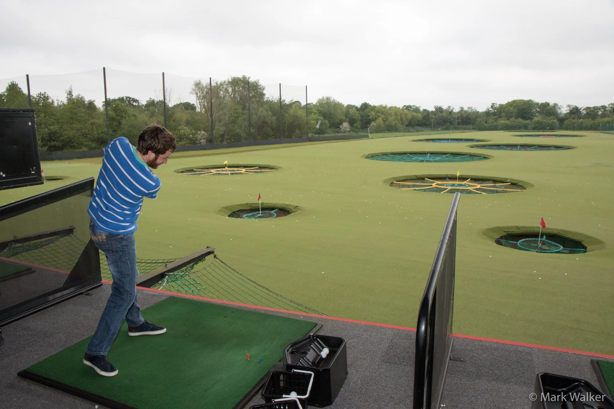 TopGolf with a man in a blue striped shirt aiming at golf holes over a green landscape near Myrtle Beach, SC