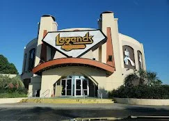 Exterior of the Legends building with a prominent sign, surrounded by trees and clear blue sky near Myrtle Beach, SC