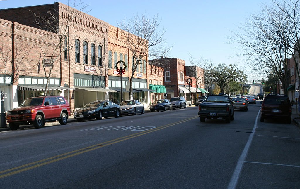 Downtown Conway, SC street scene with brick buildings, parked cars, and holiday wreath decorations on storefronts, under a clear blue sky near Myrtle Beach, SC