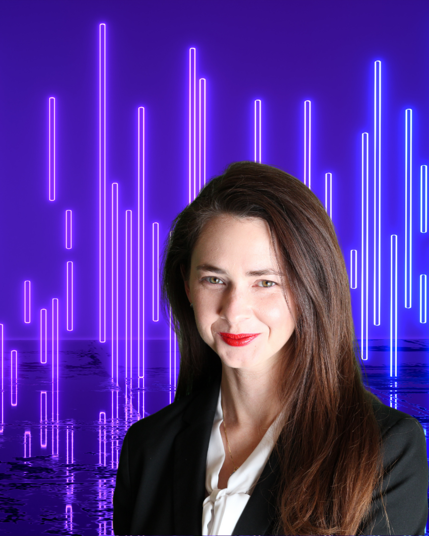 A woman with long brown hair and red lipstick smiling in front of a purple neon light display over water.