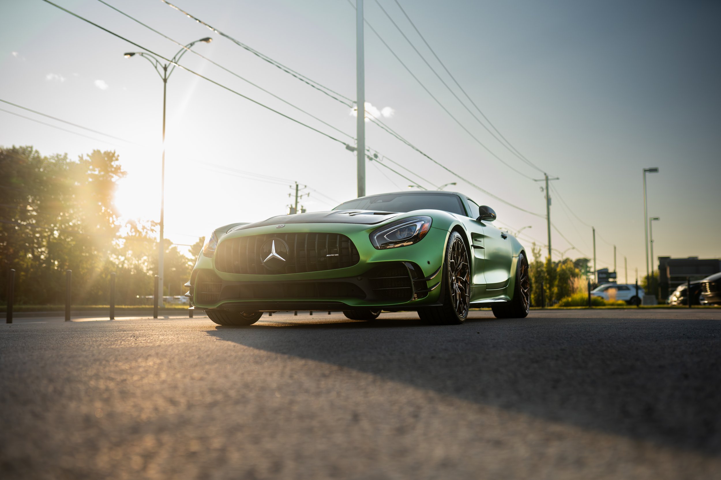 A green Mercedes-Benz sports car parked outdoors during sunset, with power lines and streetlights in the background.