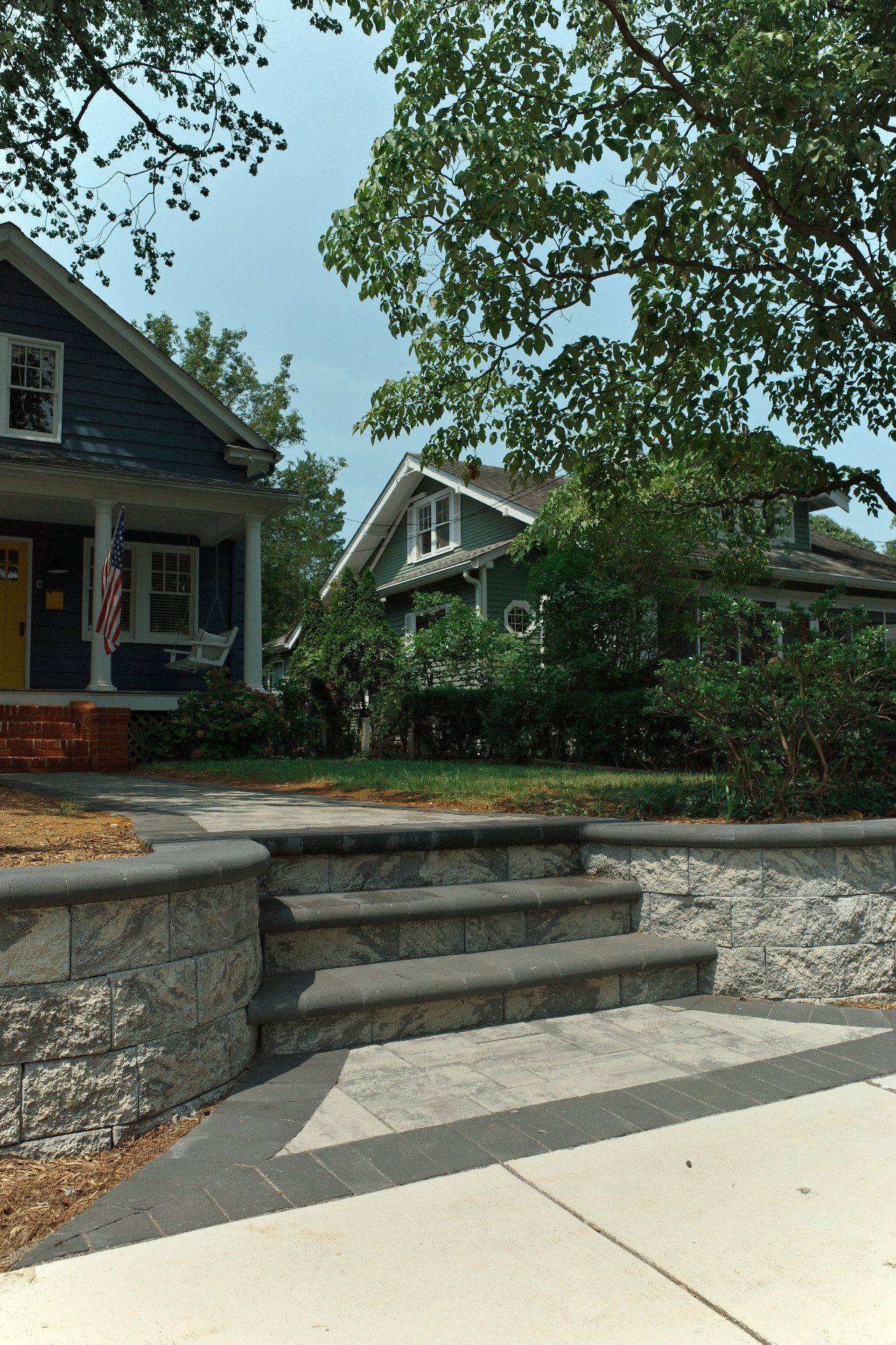 Broad paver entry steps and a block retaining wall beside a blue home.