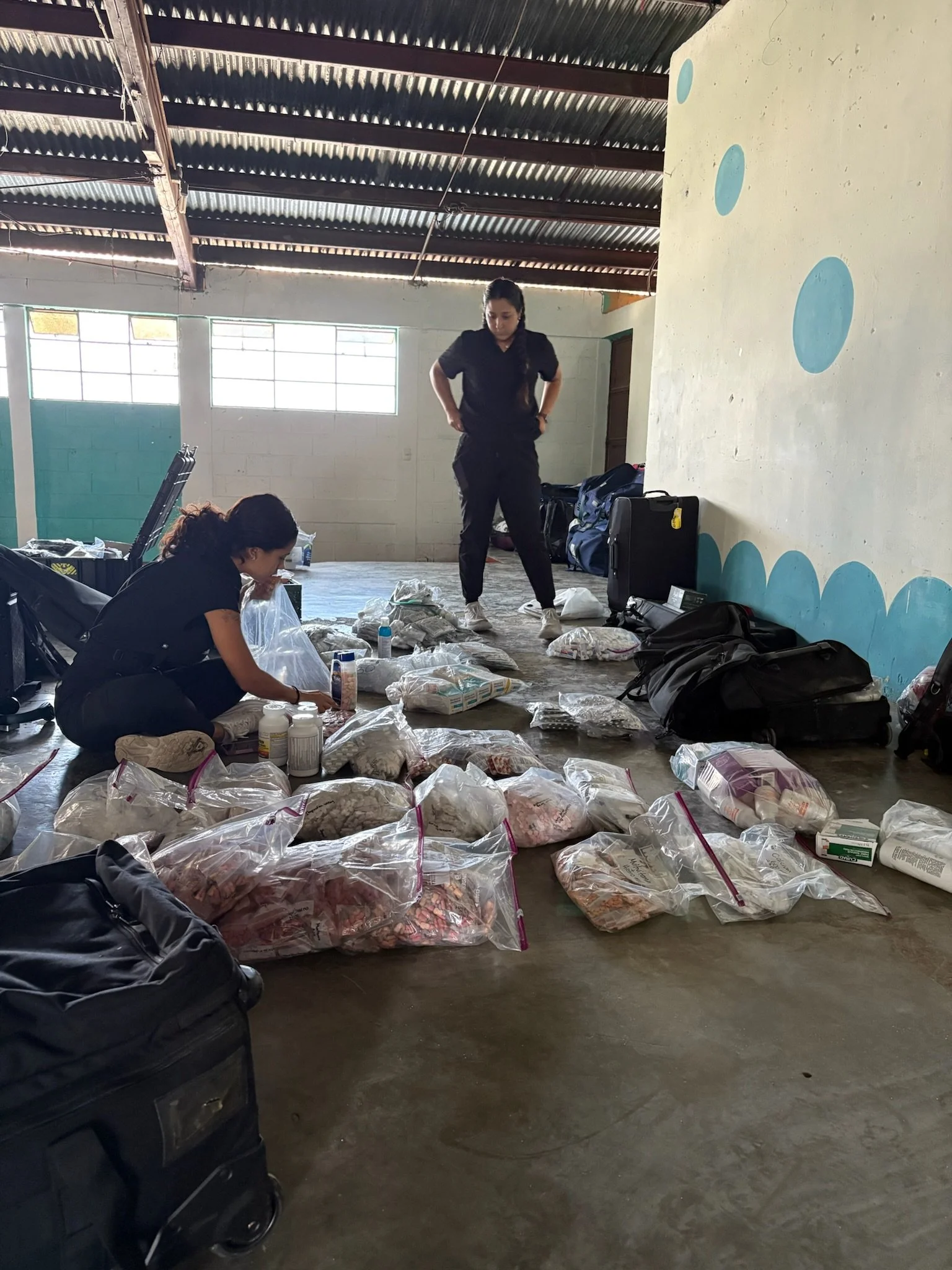 Two women preparing food supplies in an indoor space with bags of food on the floor and some luggage nearby.