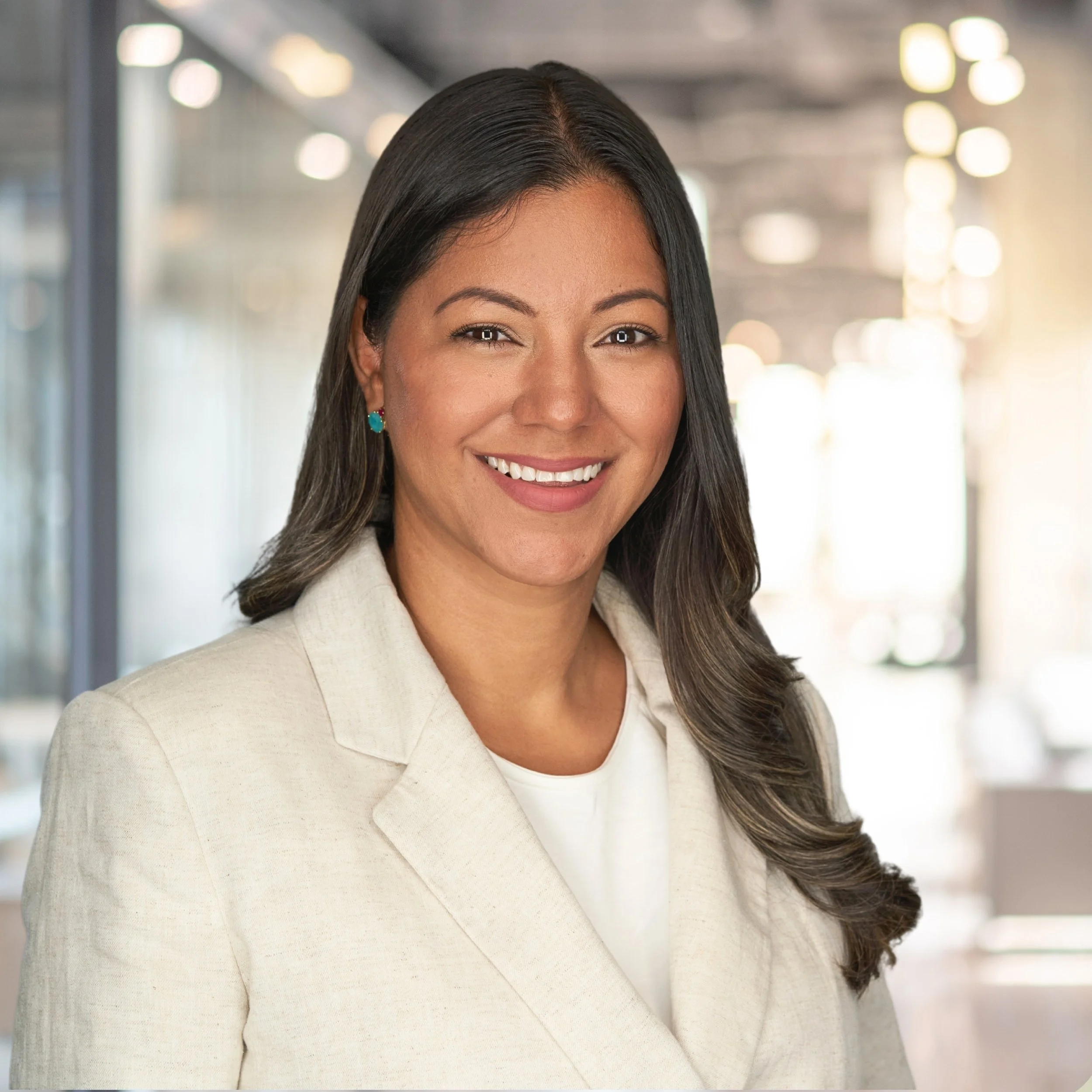 Professional woman in business attire smiling in an office setting with blurred background.