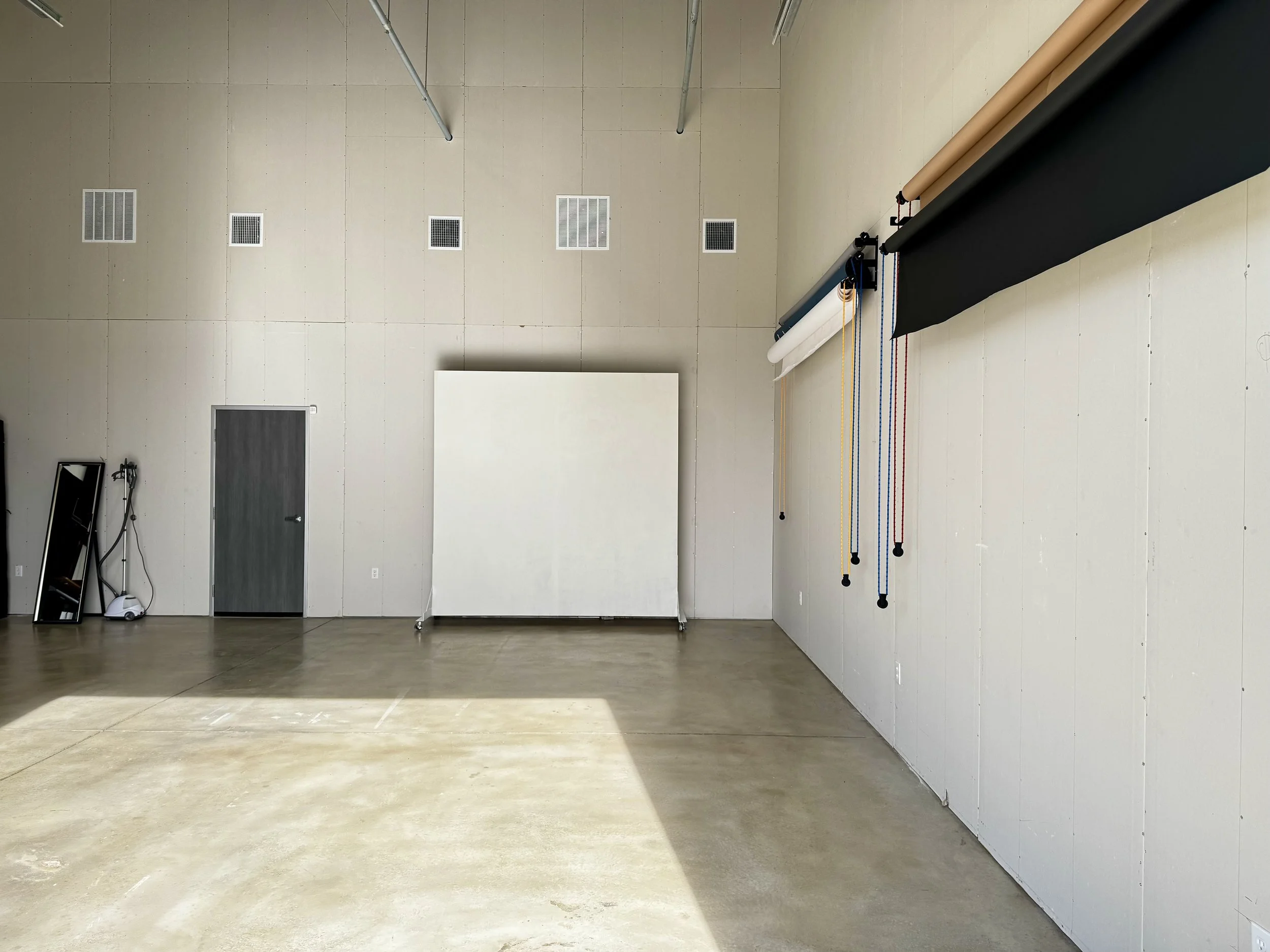 A holiday-themed photography setup with Christmas decorations including a tree, a reindeer figure, candy cane props, and festive garlands, along with studio lights and camera equipment, and a group of people gathered and conversing nearby.