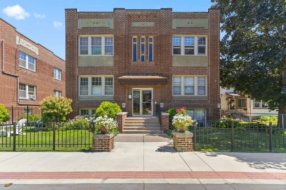 Brick two story condo building with front facing windows and potted flowers out front. one unit listed by the plourde team