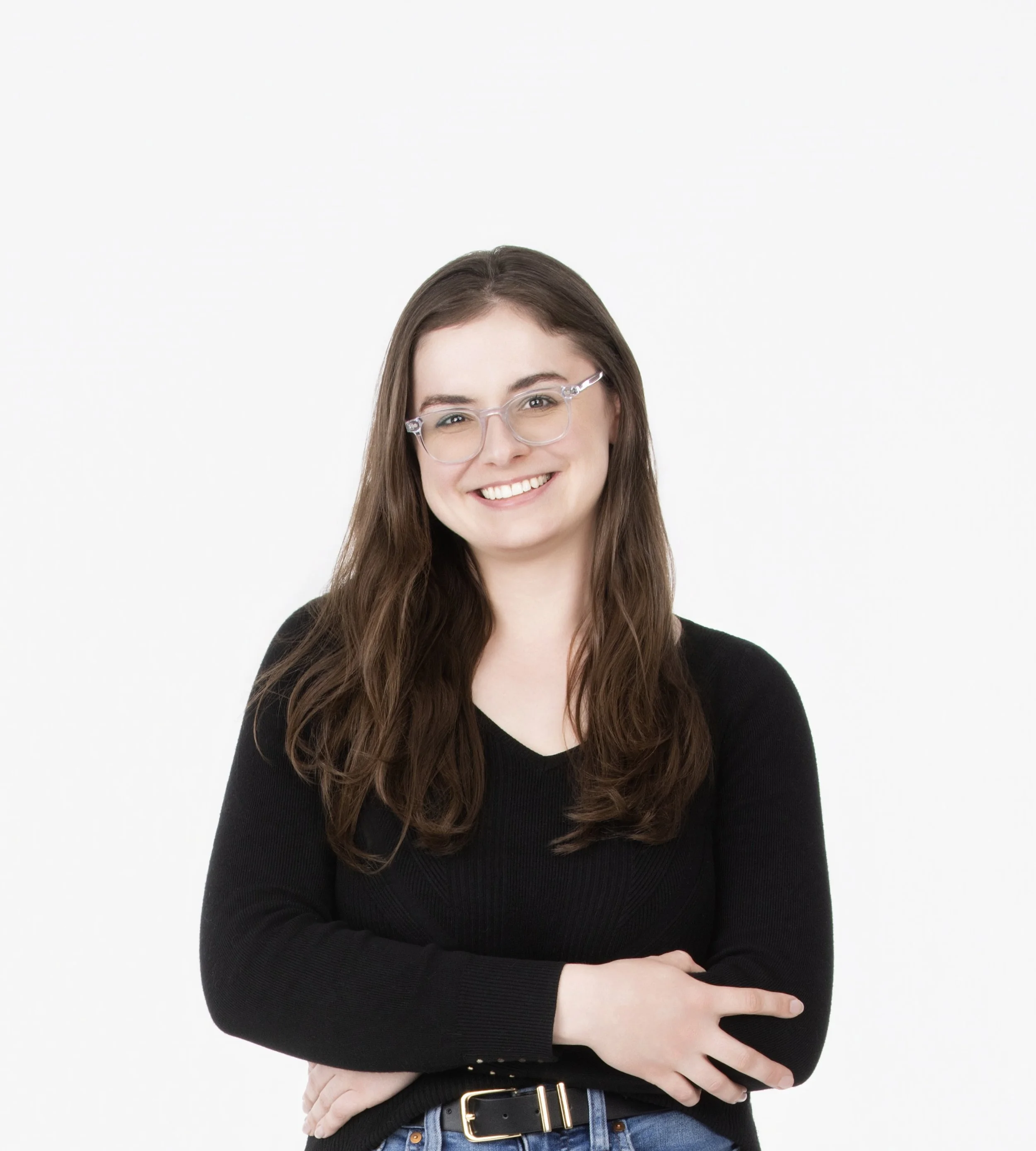 A young woman with long brown hair, wearing glasses, a black sweater, and blue jeans, against a white background. Woman is Sadie Humleker, Transaction and Office Manager of the Plourde Team.