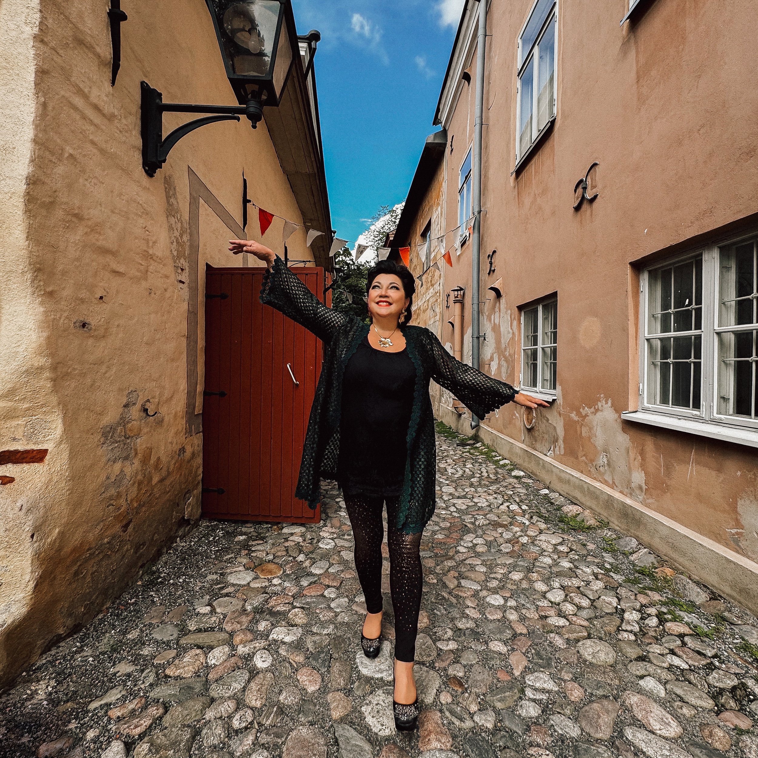 Kristiina Mäki kävelee Turussa kapealla mukulakivikujalla, taustalla on sininen taivas ja viiri.