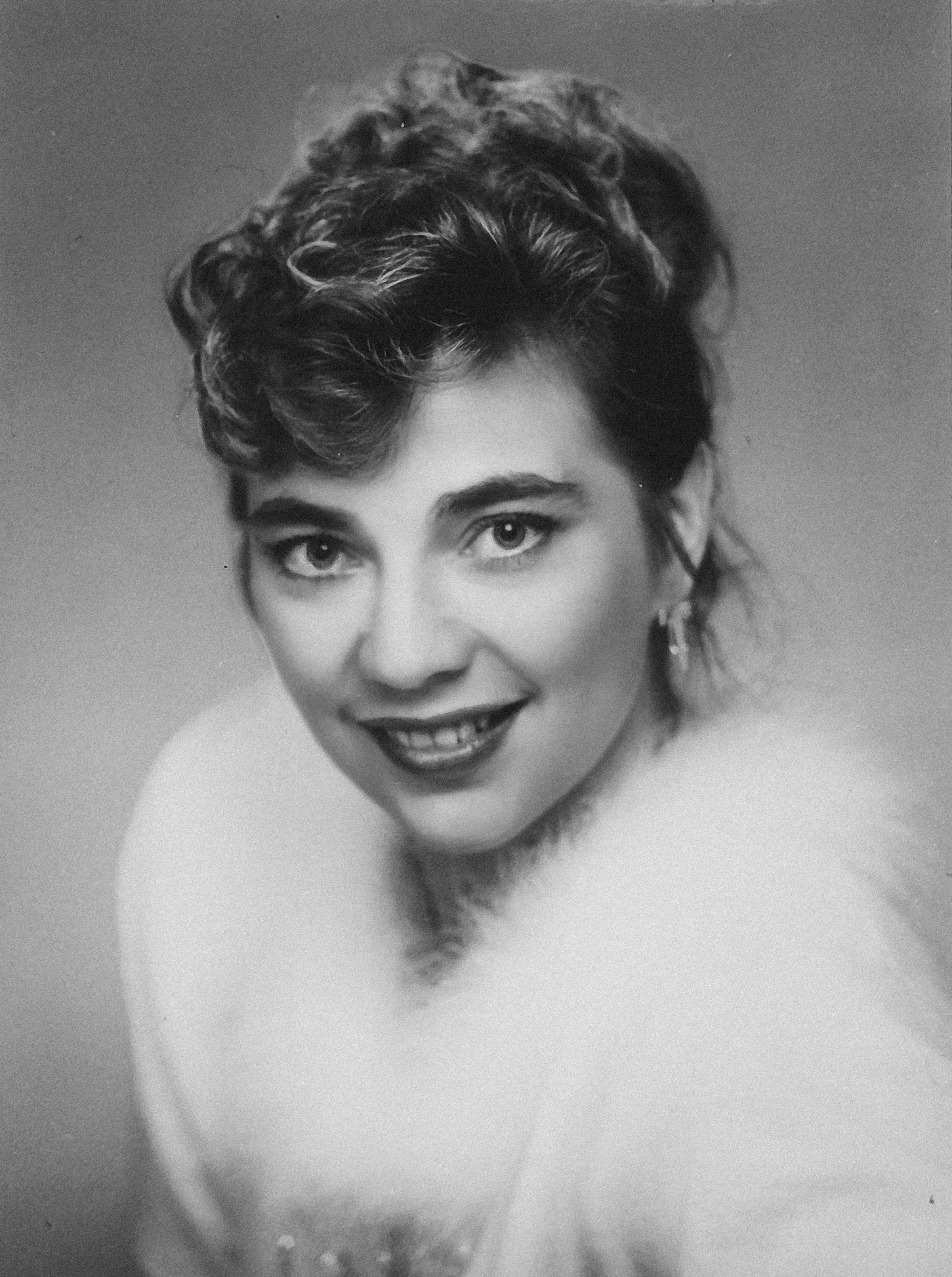 Harmaasävyinen mustavalkovalokuva Kristiina Mäestä, jolla on lyhyt, kihara tukka ja viehättävä ilme.