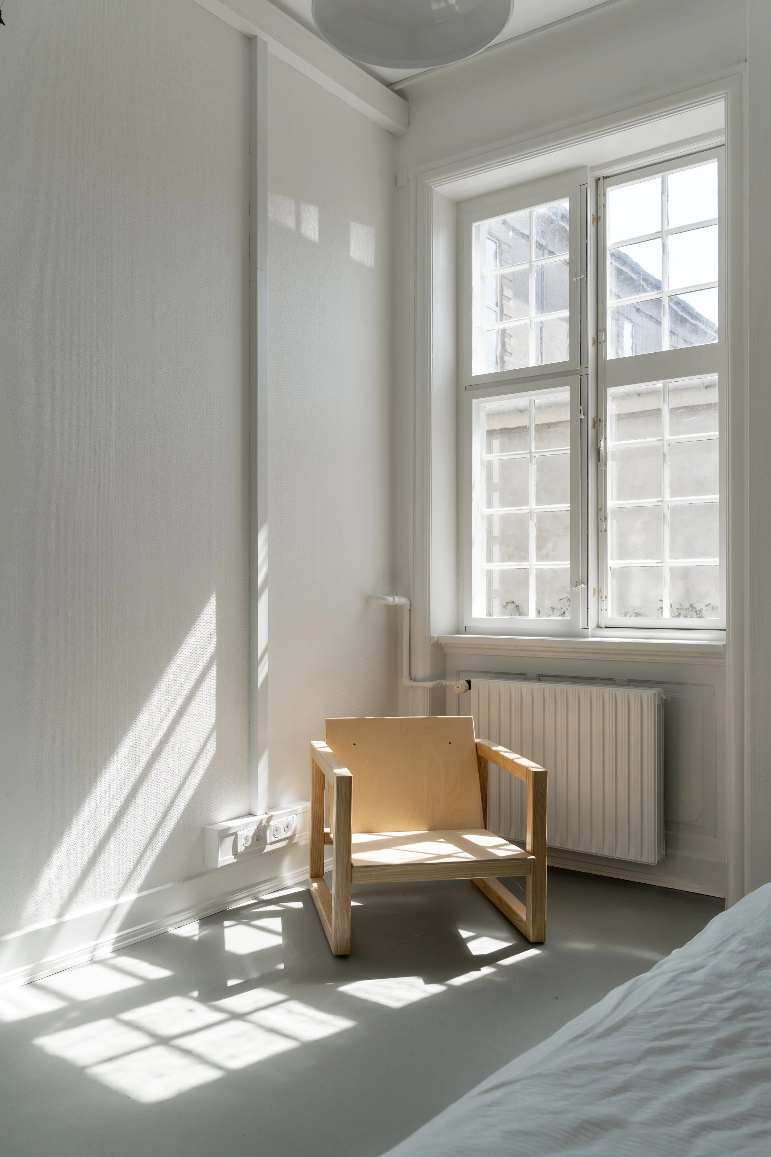 A small wooden chair placed in a corner near a window, with sunlight streaming in.