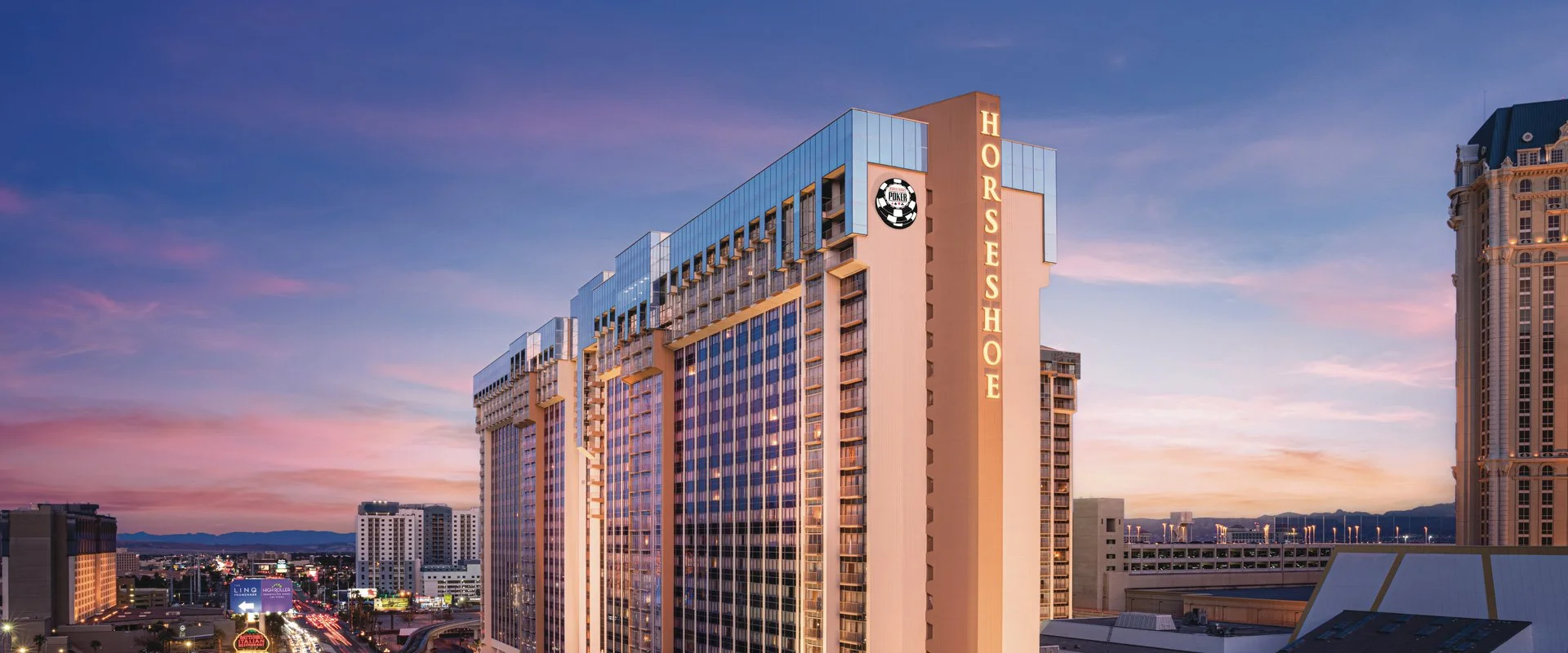 View of the Horseshoe Hotel in Las Vegas during sunset with a colorful sky and city lights below.