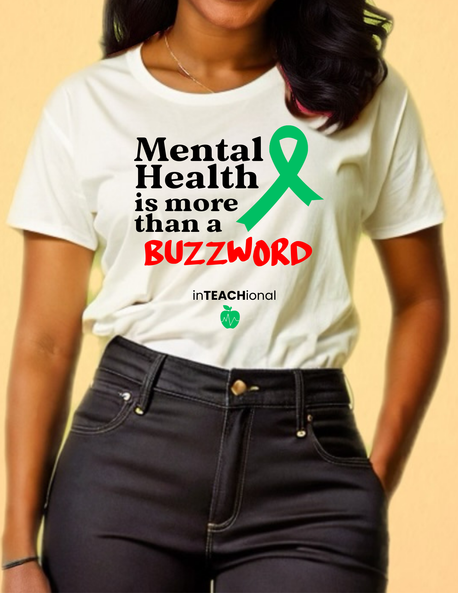 A woman wearing a white t-shirt with a green awareness ribbon, black text that reads 'Mental Health is more than a BUZZWORD', and a small green apple with a heart rate line. She is standing against a yellow background, with her hands in her black jeans pockets.