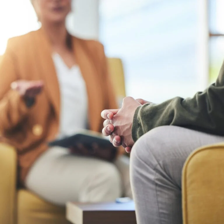 A blurred woman holding a tablet during a therapy session or counseling appointment with a client sitting across from her.