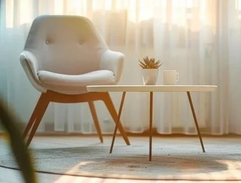 Empty modern living room with white armchair and white coffee table with a small plant, mug, and a curtain background.