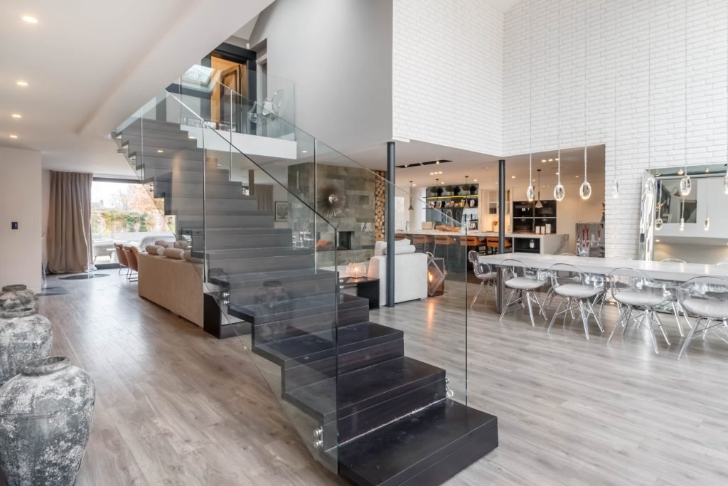 Modern open-plan interior with glass stairs, dining area, and living room