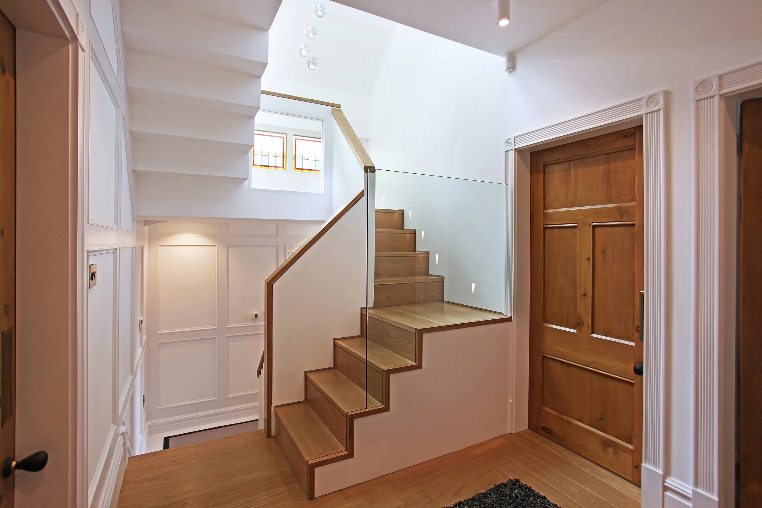 Refurbished staircase detail showing oak handrail and classic wall panelling within loft conversion and extension project.