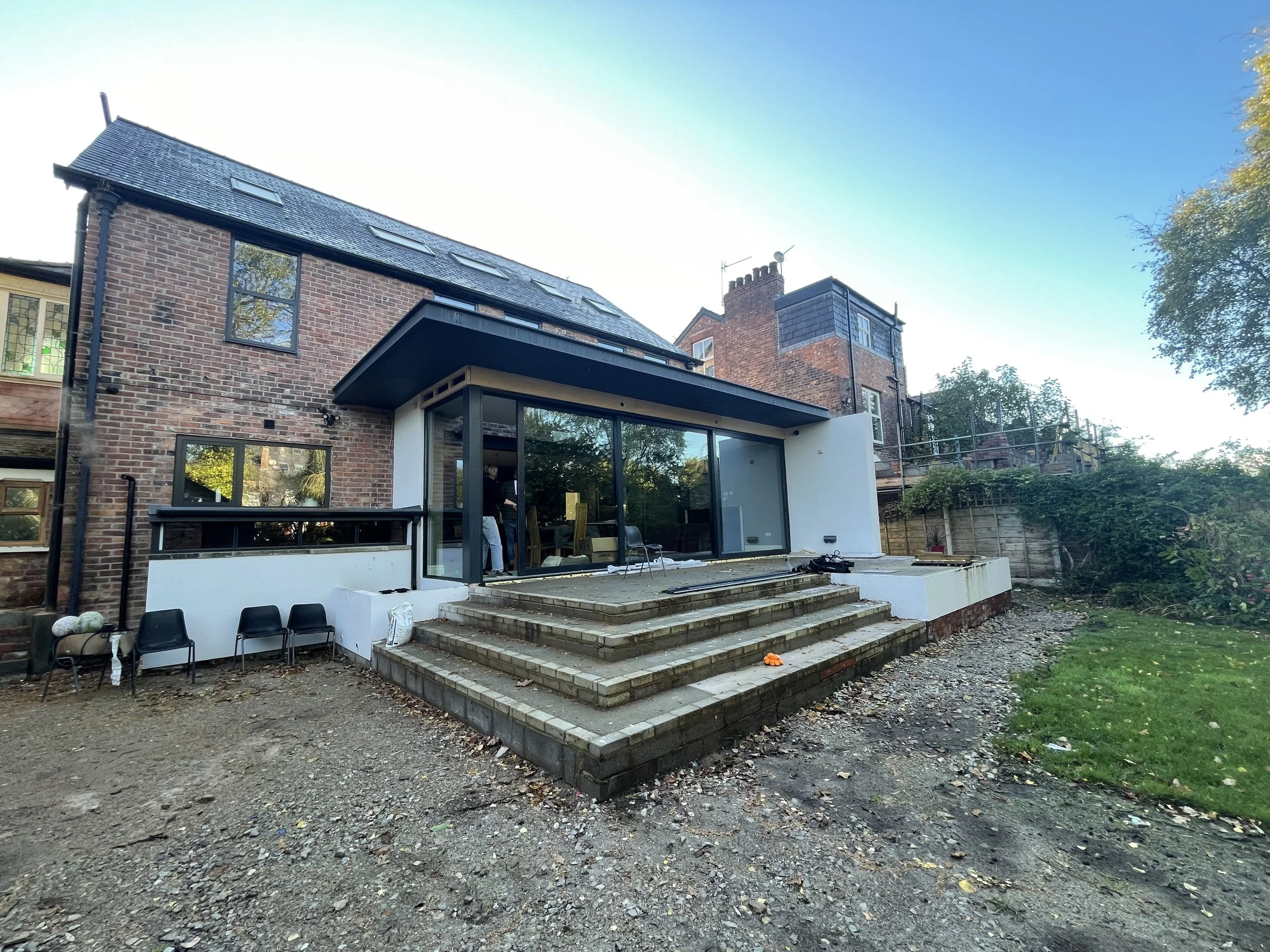 Rear extension under construction with exposed steel frame and white rendered walls on detached house in West Didsbury, Manchester.