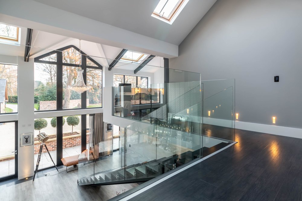 Modern interior with open space and glass staircase, featuring large windows, skylights, and neutral-colored walls.