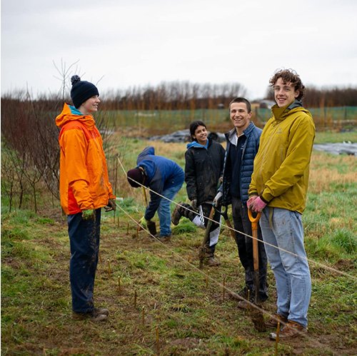 three male and two female tree planters standing in a field smiling at the camera