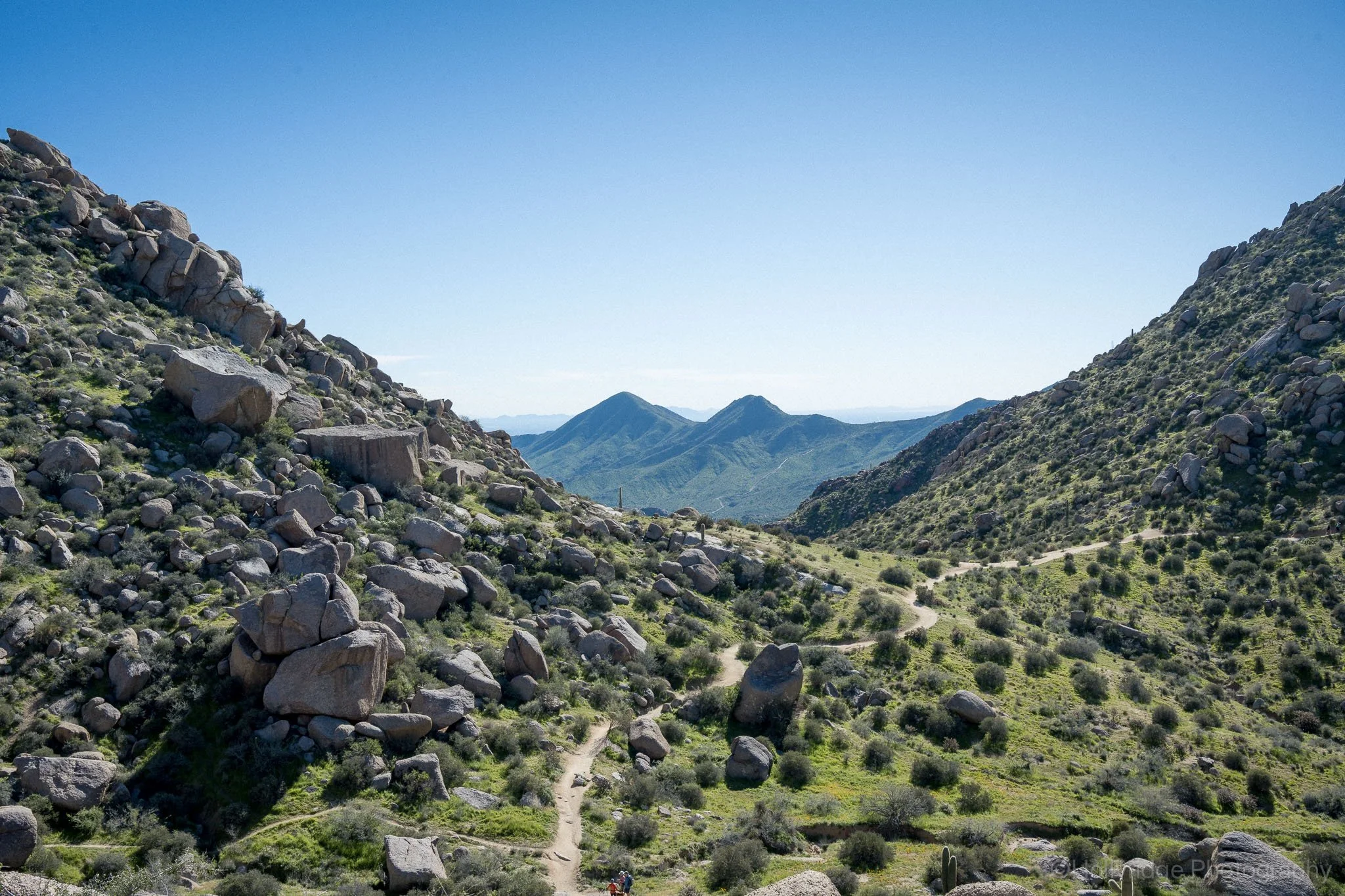 A distant hiking trail winding through two green hills strewn with boulders.