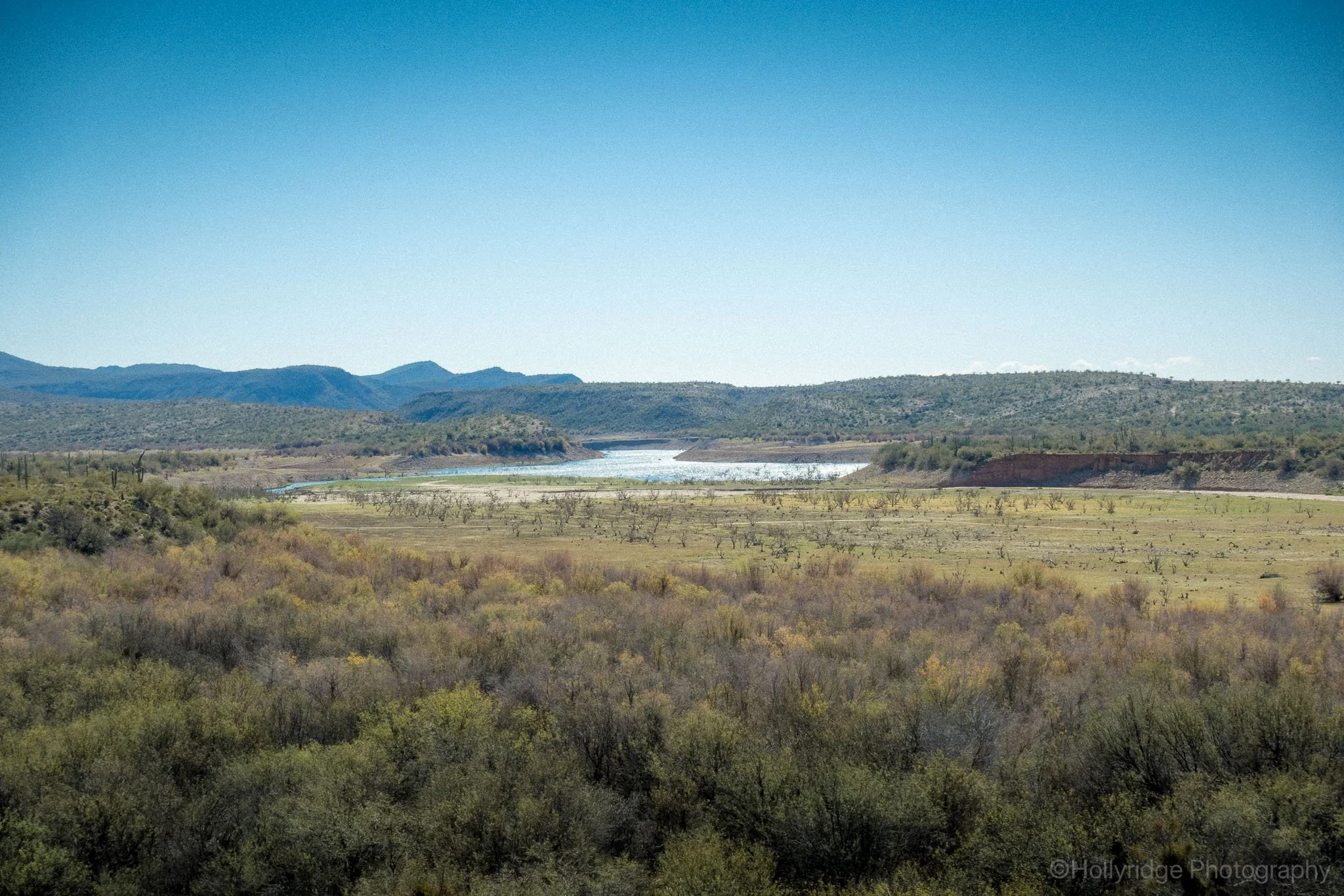 Elevated desert overlook view of Lake Pleasant in Arizona with green valley vegetation and surrounding hills under a clear blue sky.
